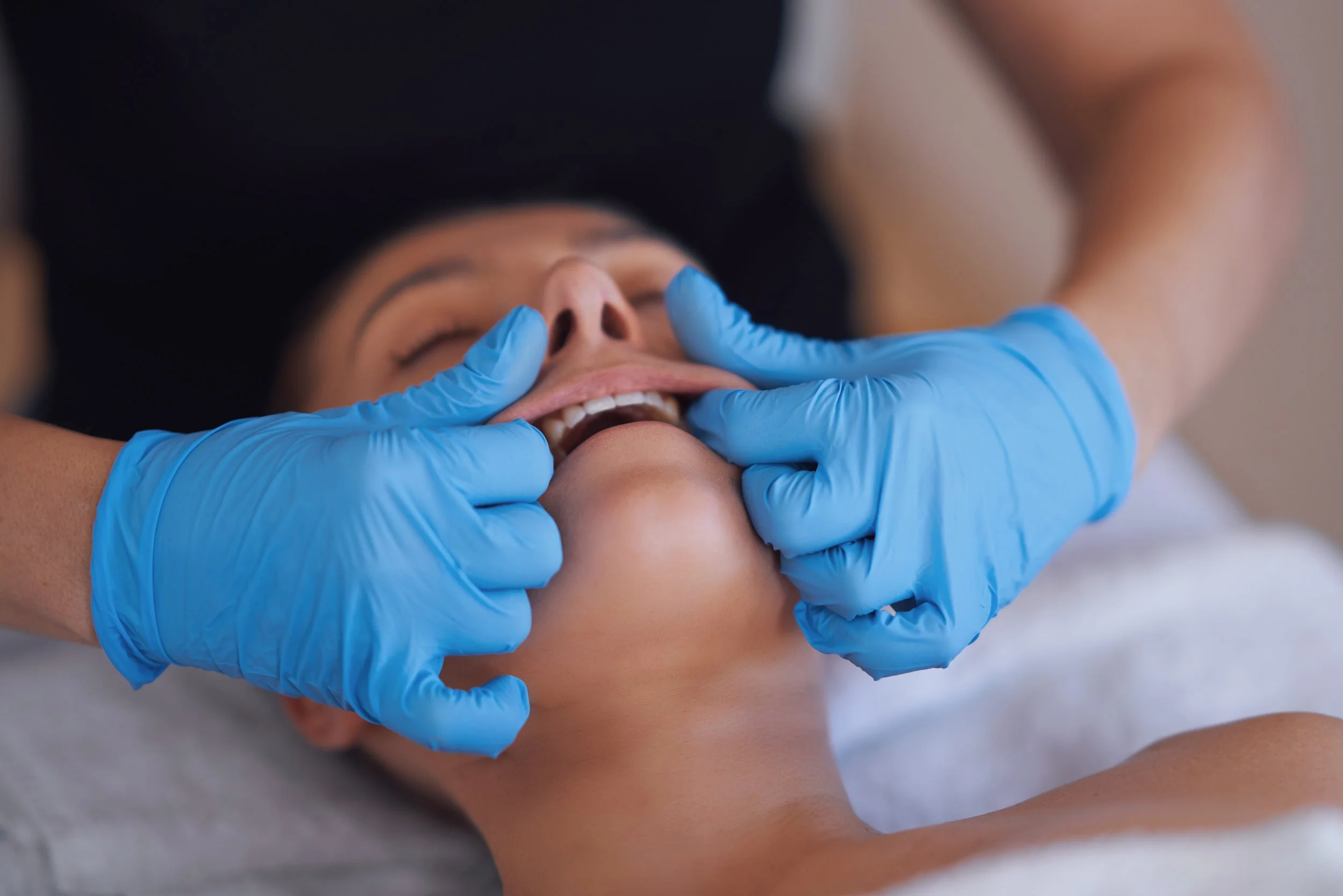A person receiving a cosmetic or medical treatment involving the mouth, with a healthcare professional wearing blue gloves.