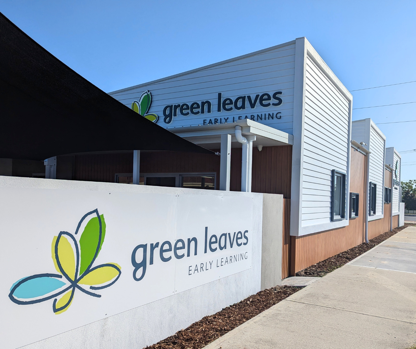 Exterior view of a building with a sign that reads 'green leaves EARLY LEARNING' and a logo of a butterfly with green, yellow, and blue wings.