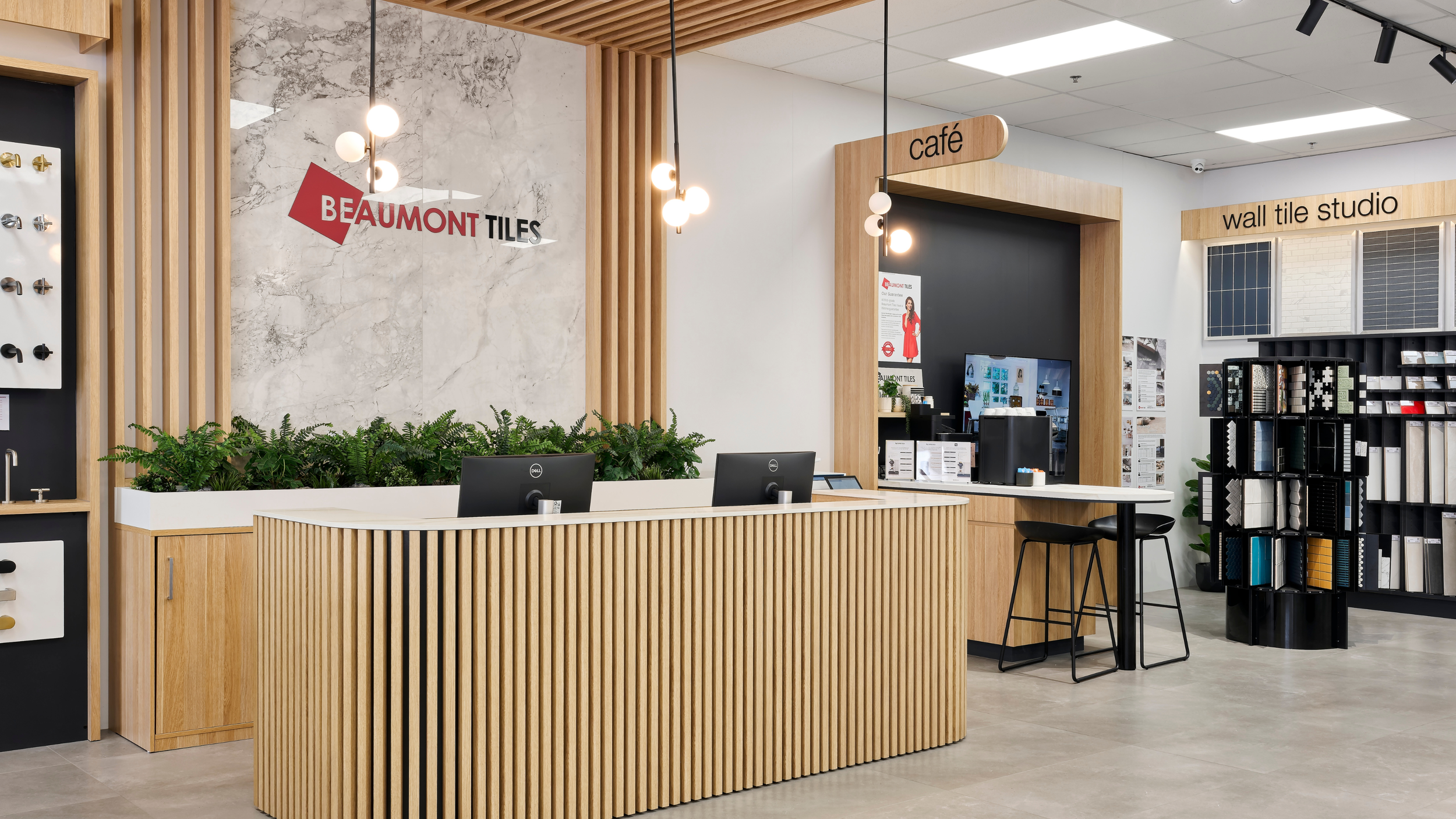 Interior of a building materials showroom with a reception desk, display samples, and signage for Beaumont Tiles, café, and wall tile studio.