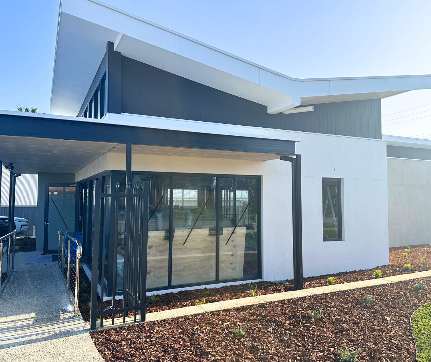 Modern two-story house with white and dark gray exterior, large glass windows, and a small gated entrance, under a clear blue sky.