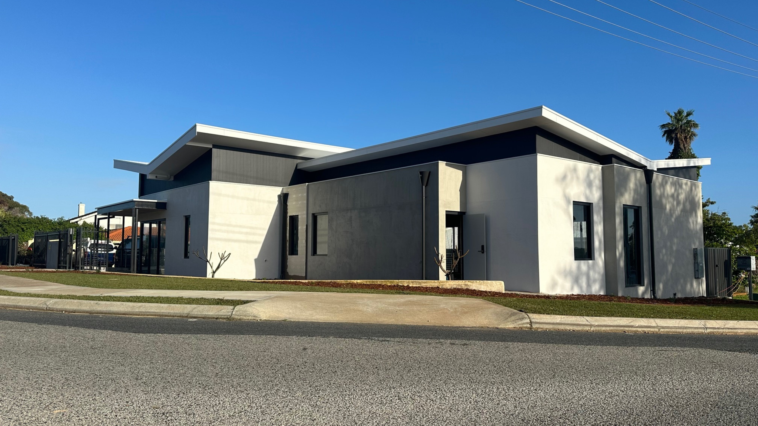 Modern building with white and dark gray exterior walls, multiple windows, and a sloped roof, set against a clear blue sky.