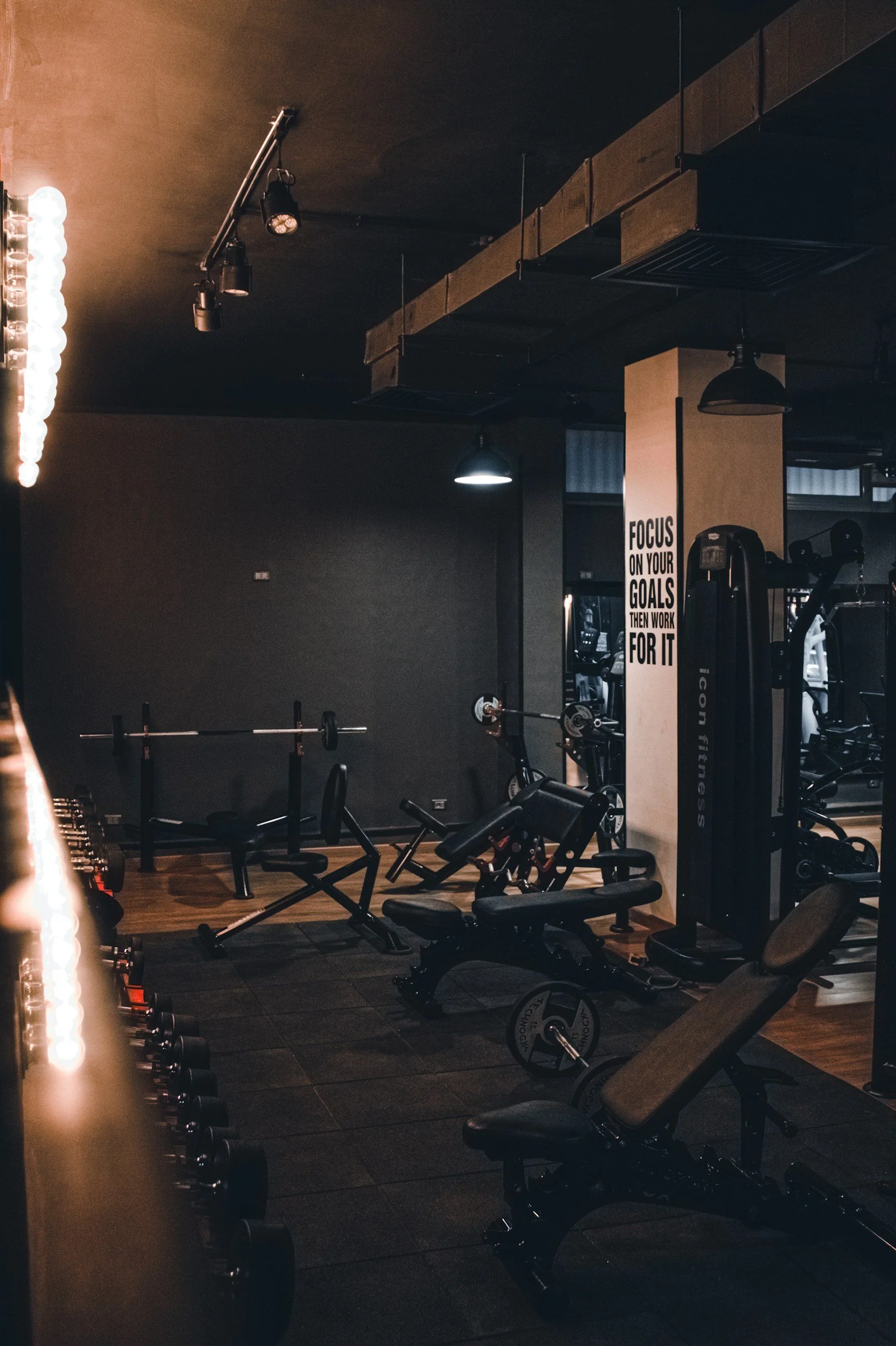 Interior of a gym with various workout equipment, including benches, weight racks, and a motivational sign on the wall that reads, 'Focus on your goals then work for it.'