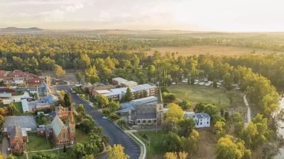 Aerial view of a small town with houses, trees, and roads surrounded by green landscape and open fields