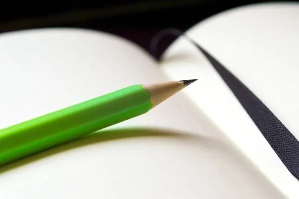 Close-up of a green pen resting on an open blank notebook or journal.