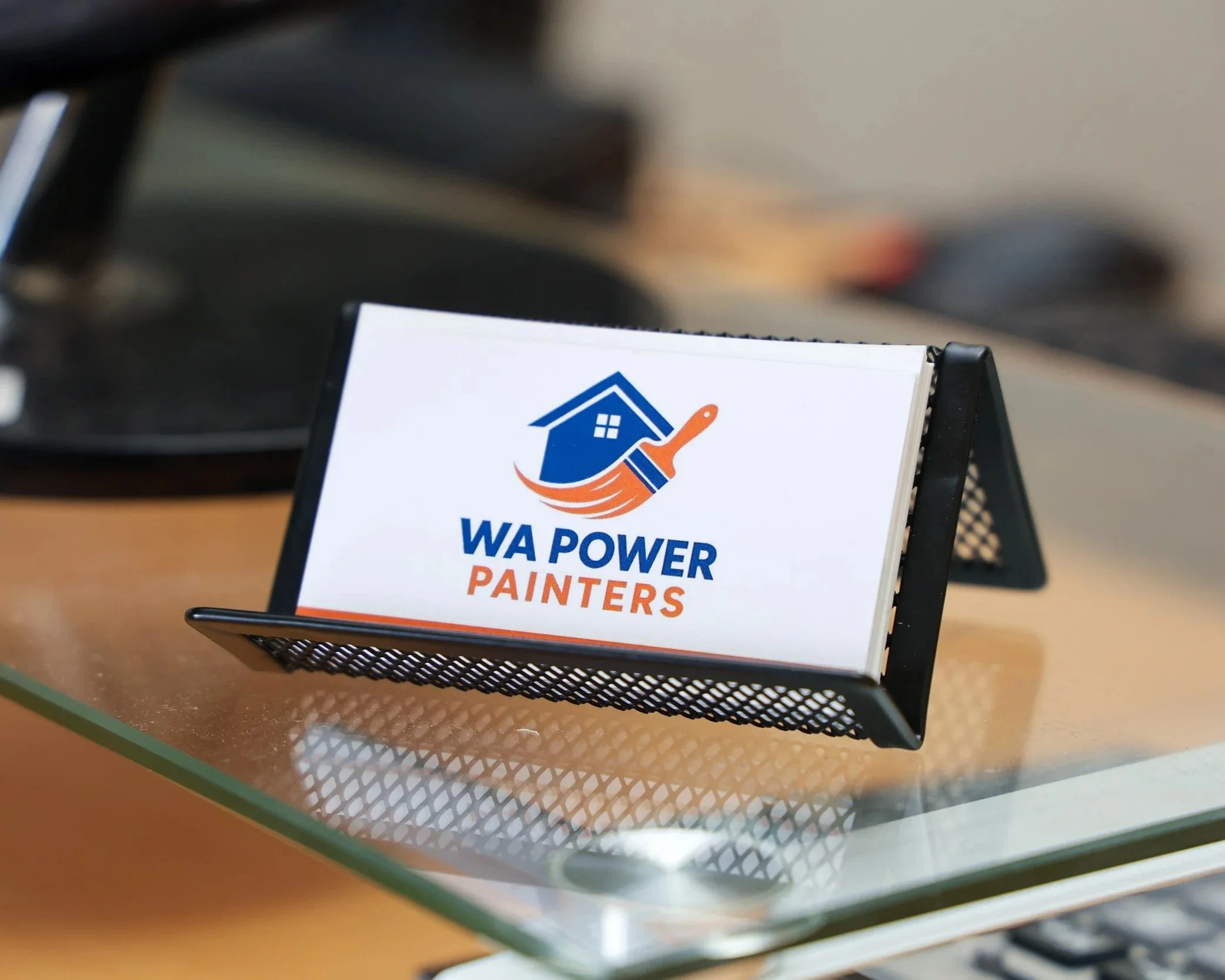 Business card for WA Power Painters on a desktop with computer monitor in the background.