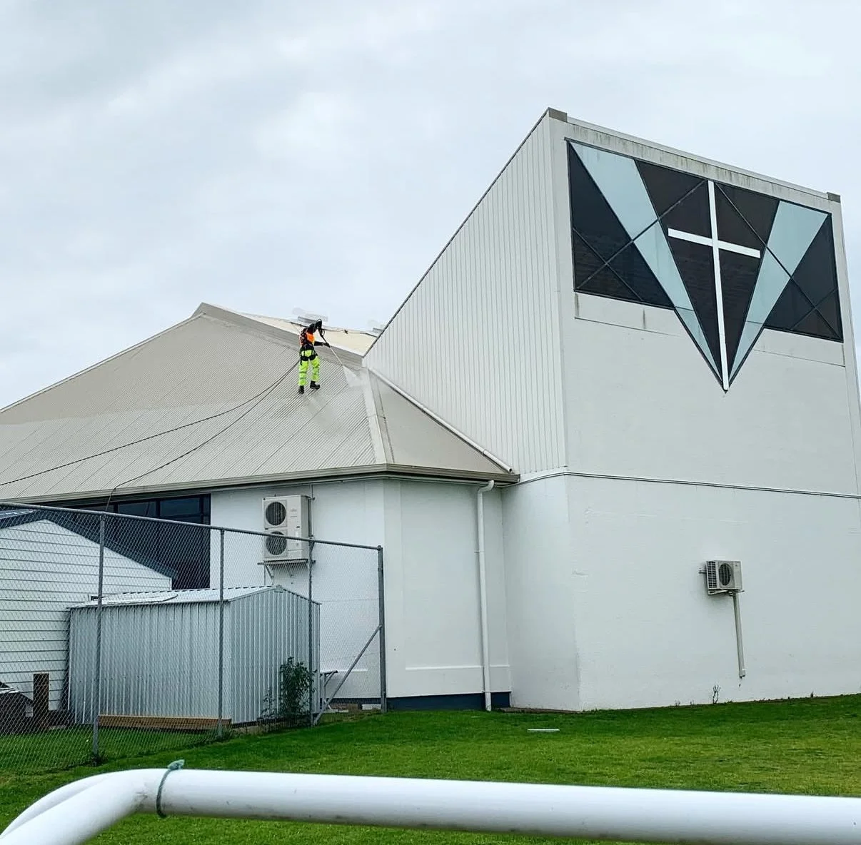 Worker cleaning or inspecting the roof of a white building with a large geometric diamond-shaped logo on the wall.