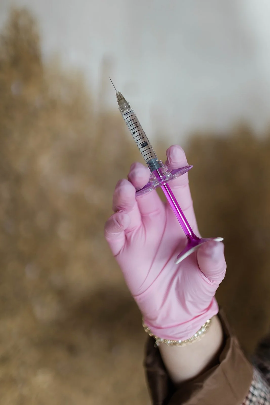 A gloved hand holding a syringe filled with pink liquid.