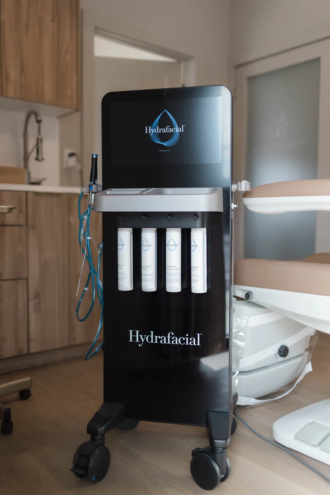 Hydrafacial machine with display screen and bottles for skincare treatment in a clinic setting.