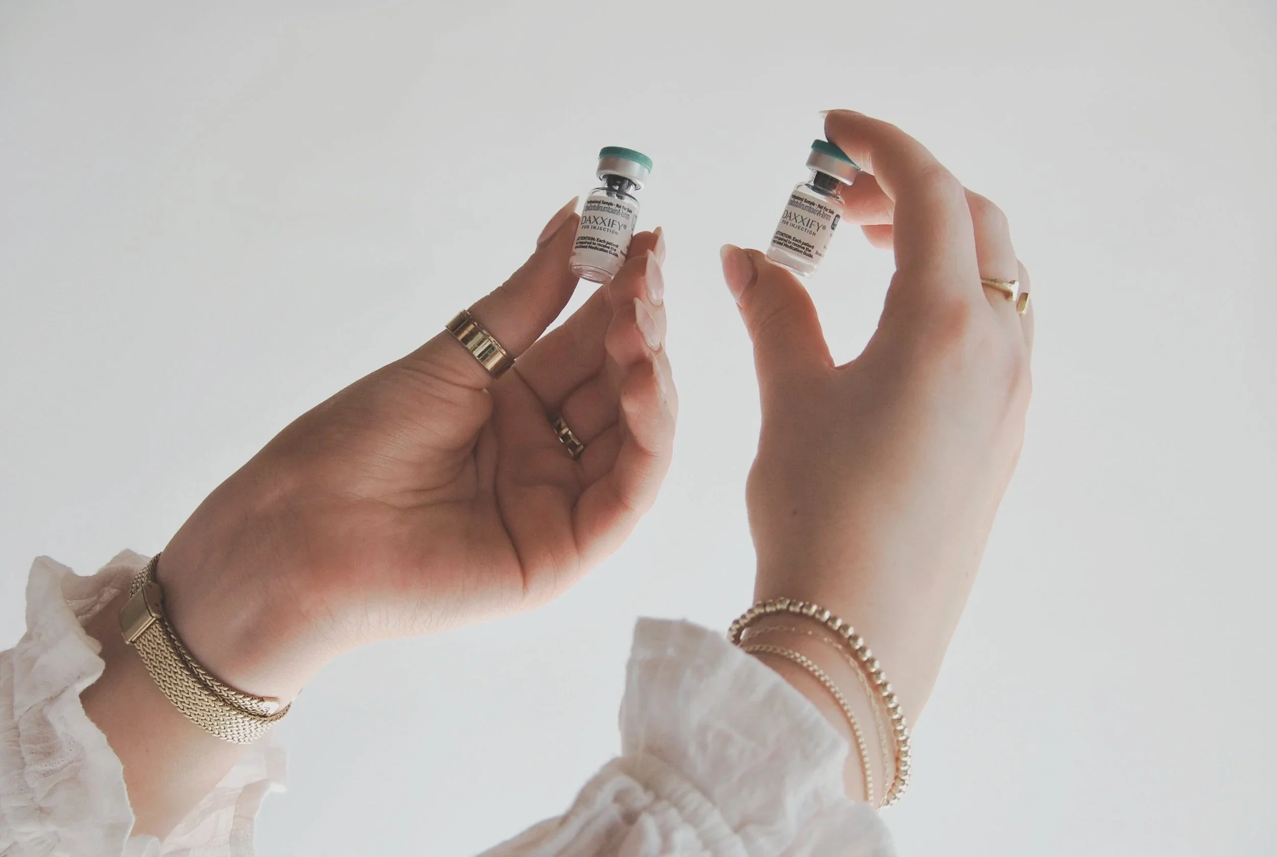 Two hands each holding a small vial labeled 'DAXIFY' with white background.