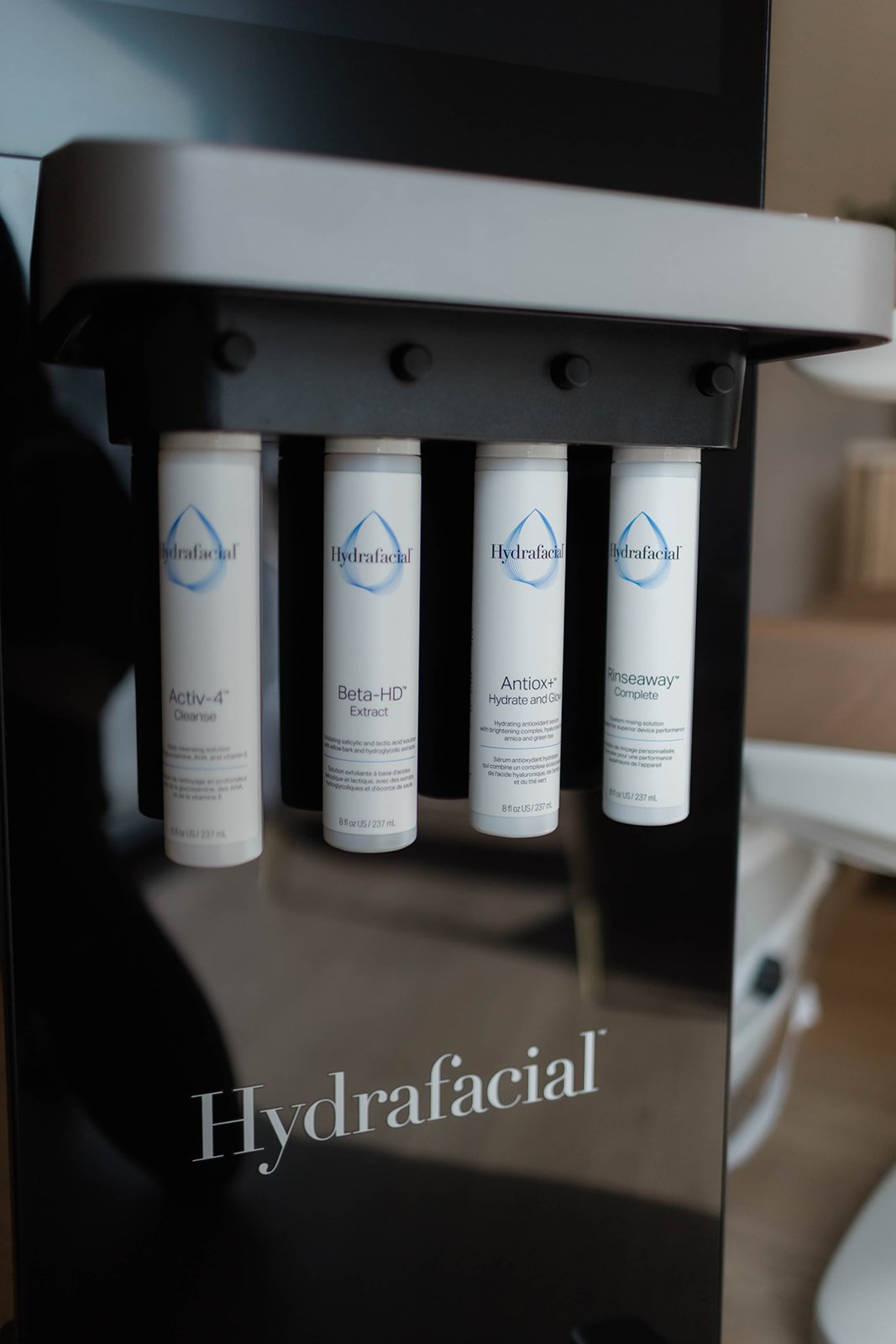 A Hydrafacial machine with four labeled skincare serum bottles visible inside the device.