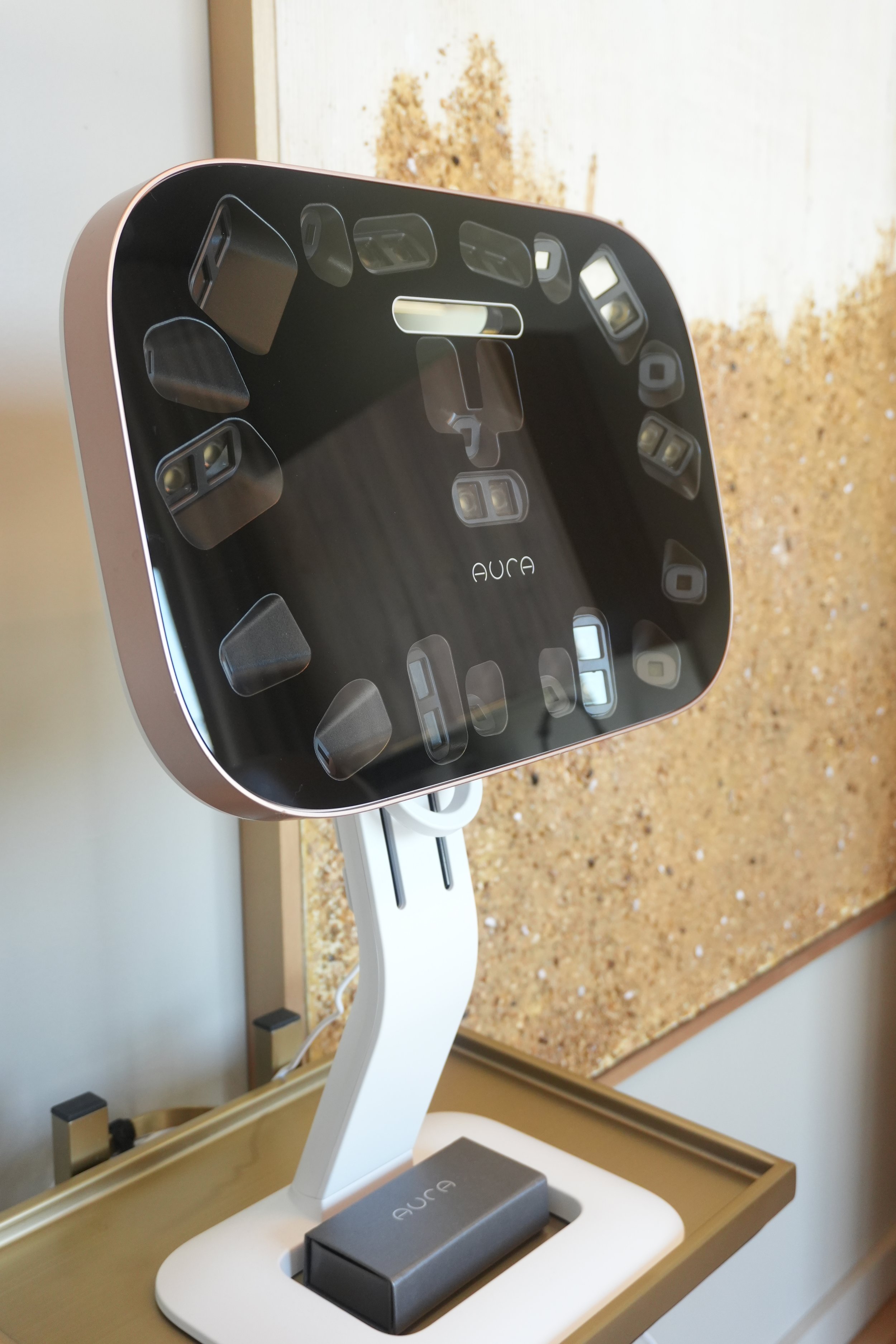 A modern Aura brand desktop dental x-ray machine with various sensors and attachment ports, placed on a wooden table with a granite countertop in the background.