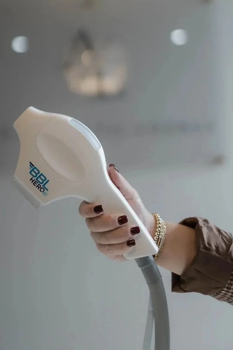 A hand holding a laser hair removal device labeled 'BBL Hero' against a reflective ceiling with a chandelier.