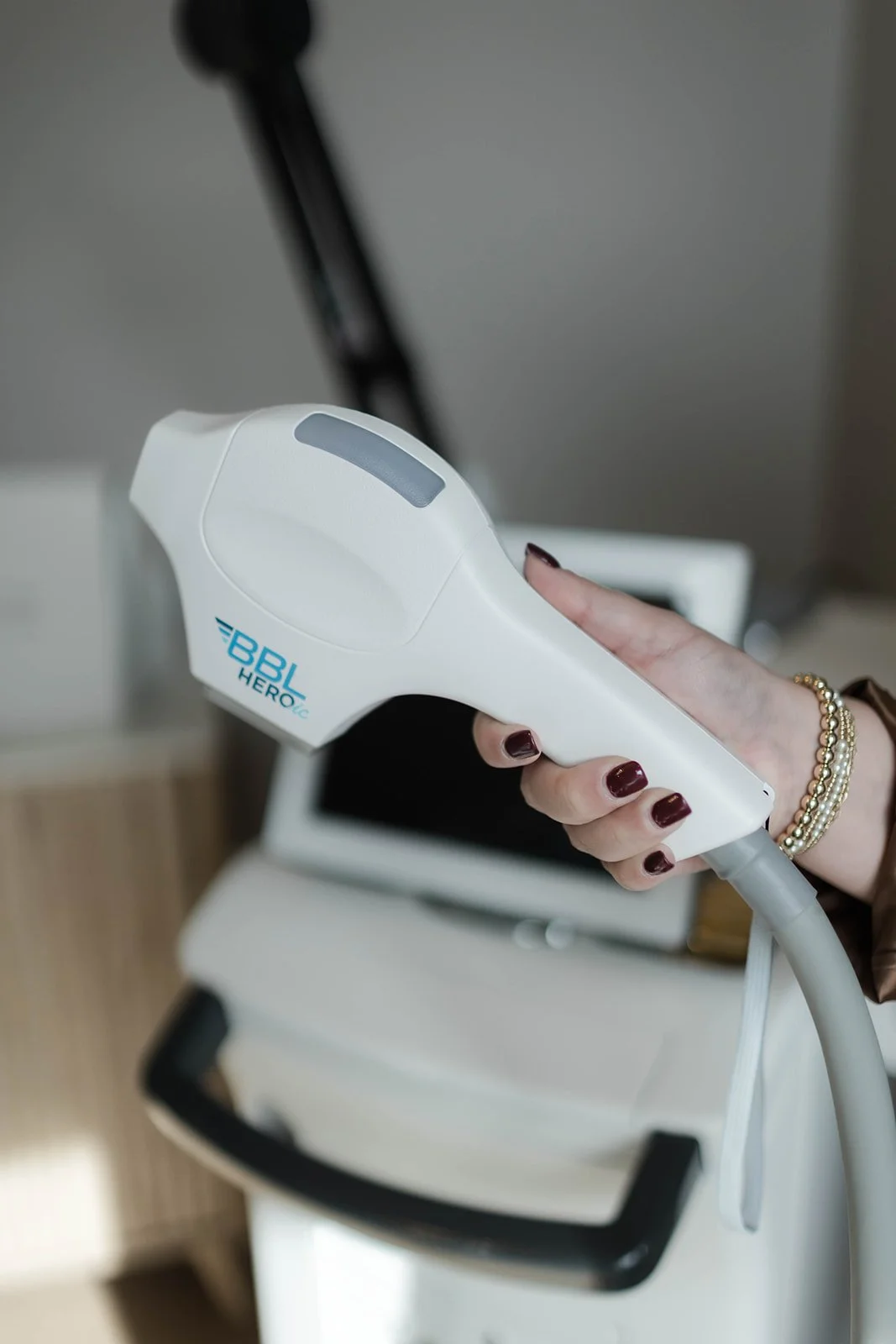 A hand holding a white handheld medical device labeled 'BBL HER Option' in front of a computer monitor on a desk.