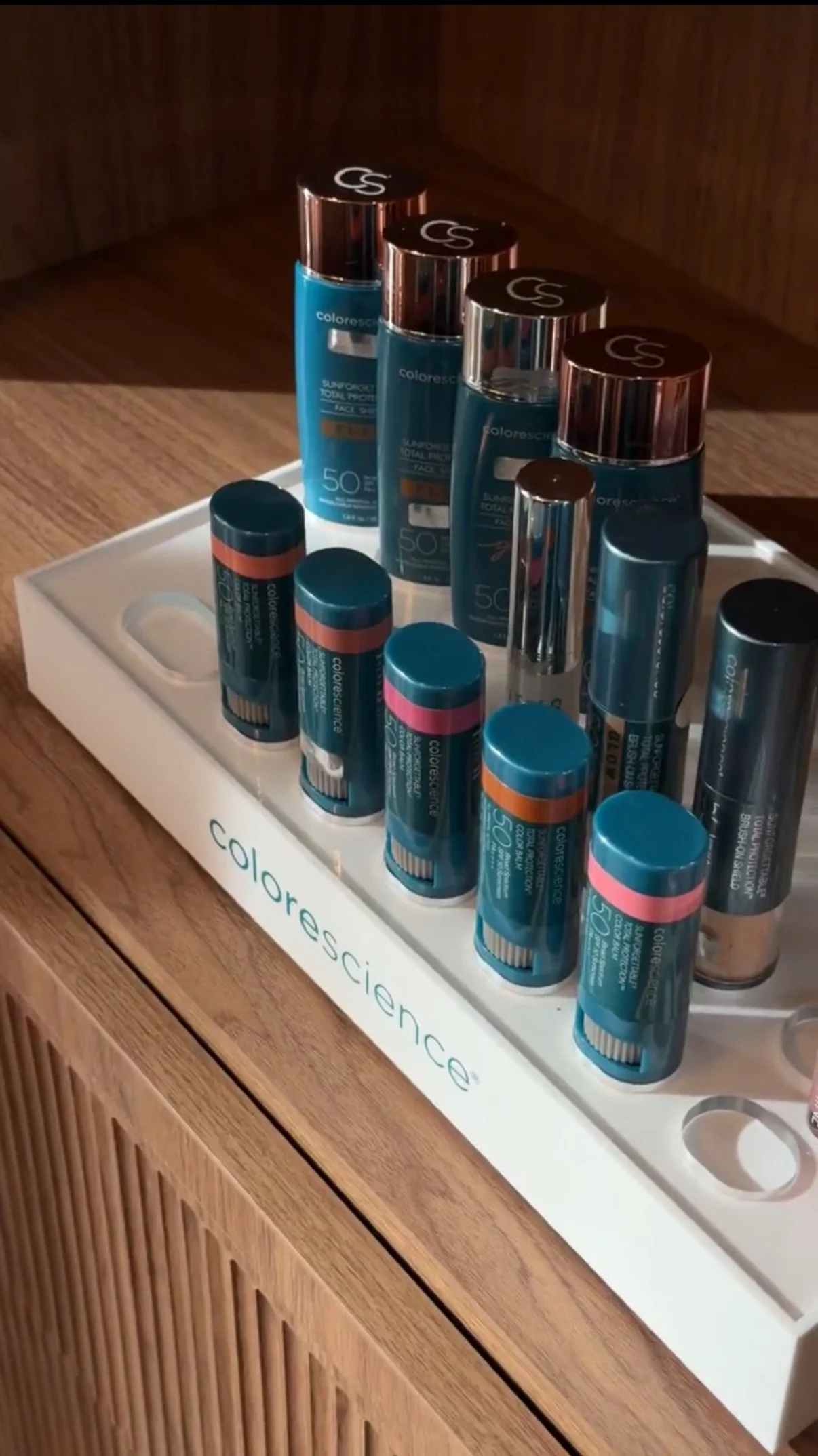 Collection of skincare products, including sunscreen sticks and bottles, organized on a white tray with the brand name 'colorescience' visible.