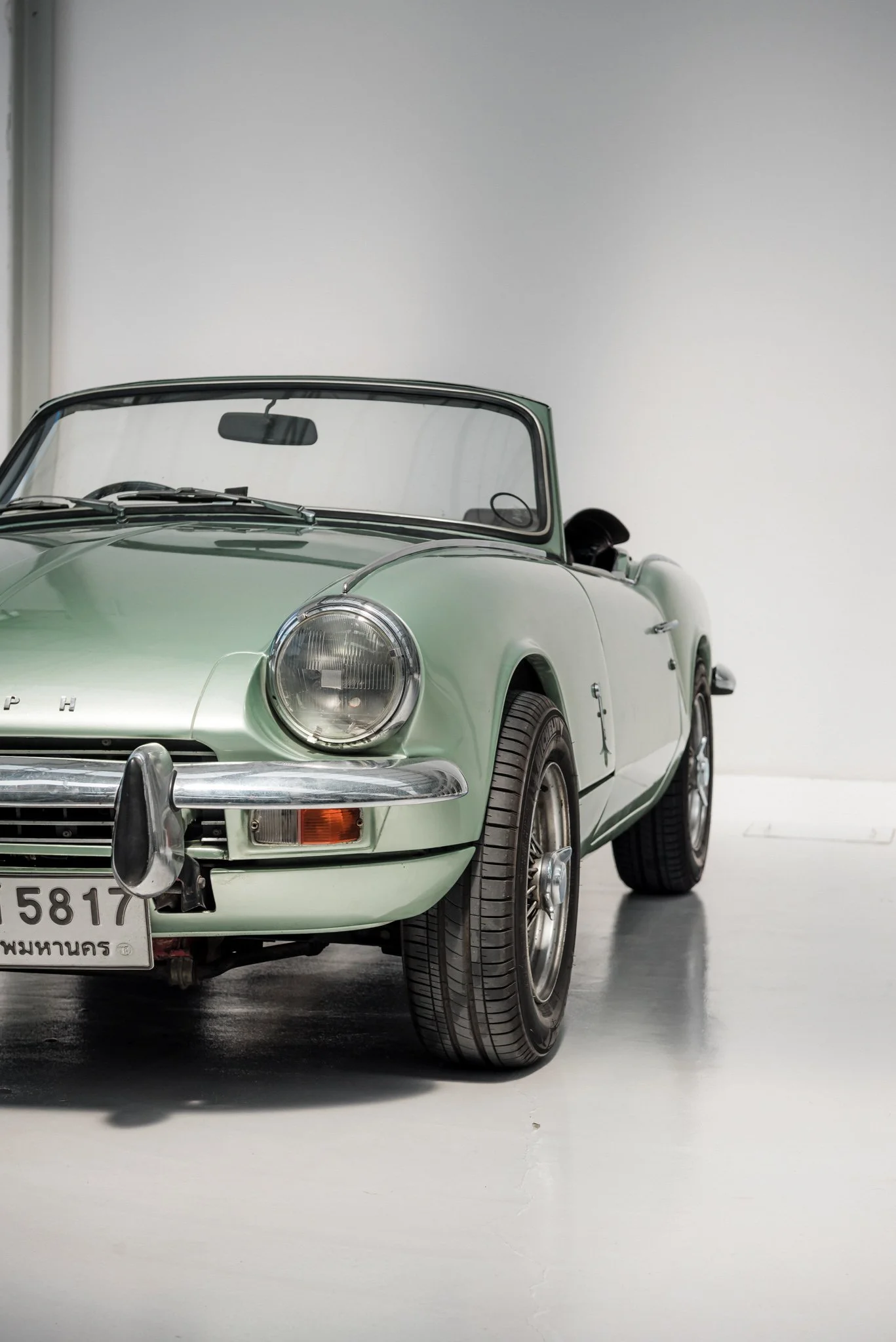 A vintage light green convertible Triumph with a classic design displayed in a gallery setting.