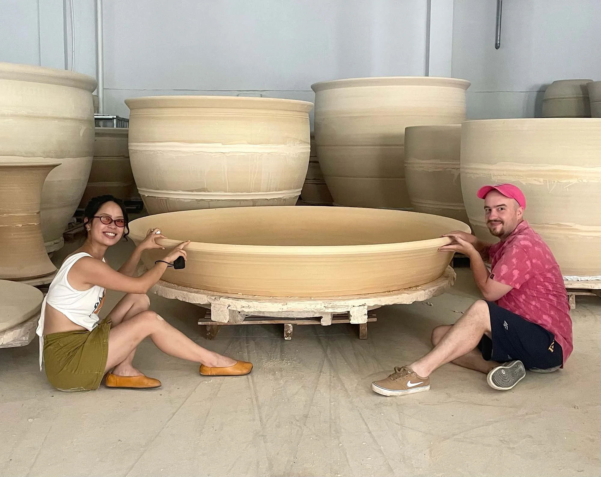 female and male beside oversized porcelain vessels in Jingdezhen.