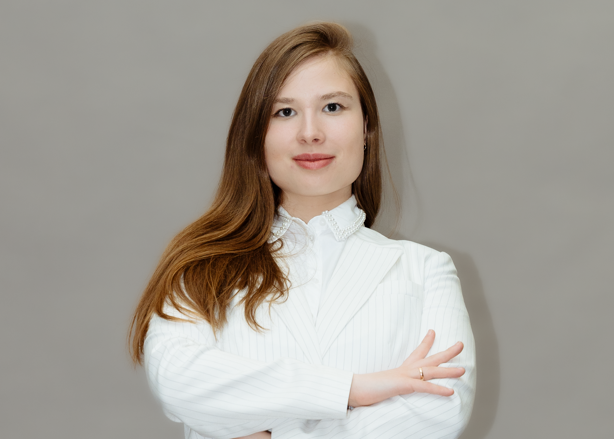 Ein junges Mädchen mit roten Haaren, das einen weißen Blazer trägt, posiert vor einem grauen Hintergrund.