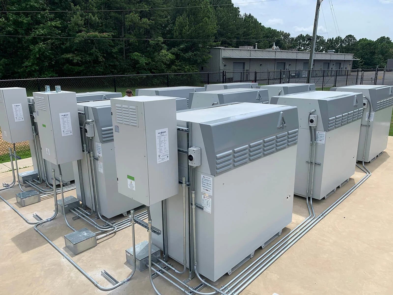 Multiple large industrial HVAC units installed outside on a concrete surface, with electrical wiring connected to each unit.