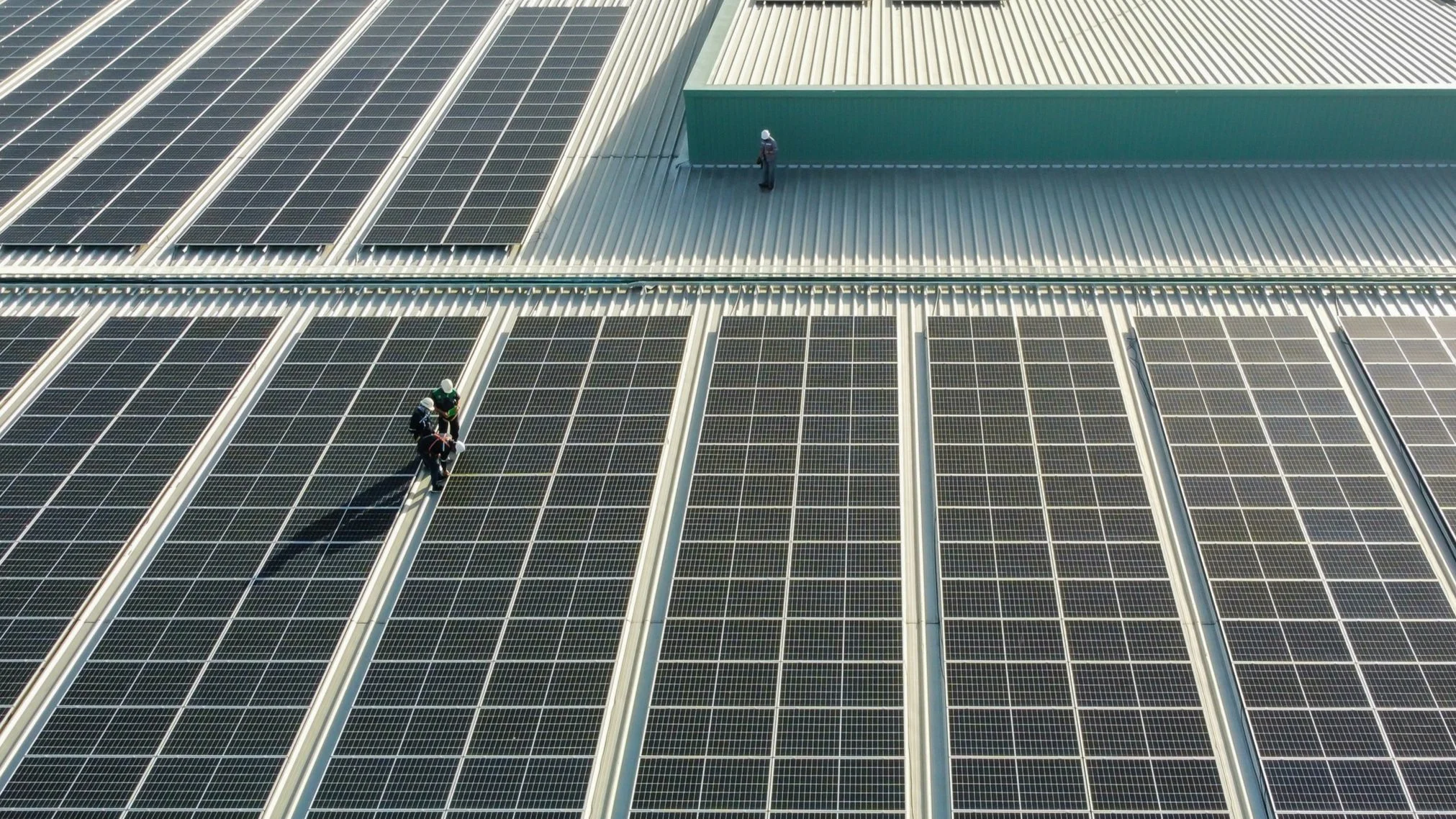 Workers inspecting solar panels on a large industrial rooftop.