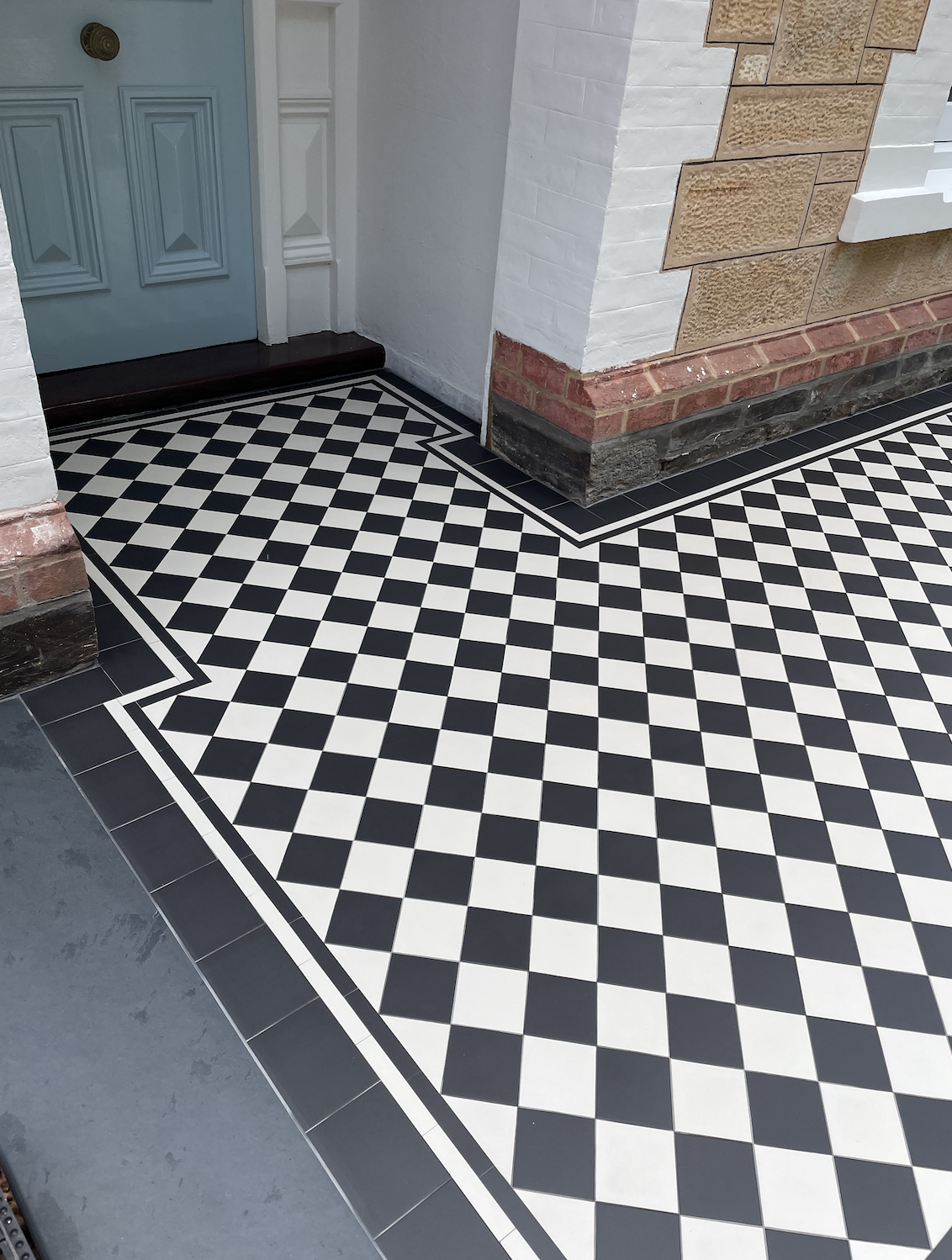 Black and white checkered tile flooring near a light blue door with white trim, adjacent to a wall with decorative brick and stone accents.