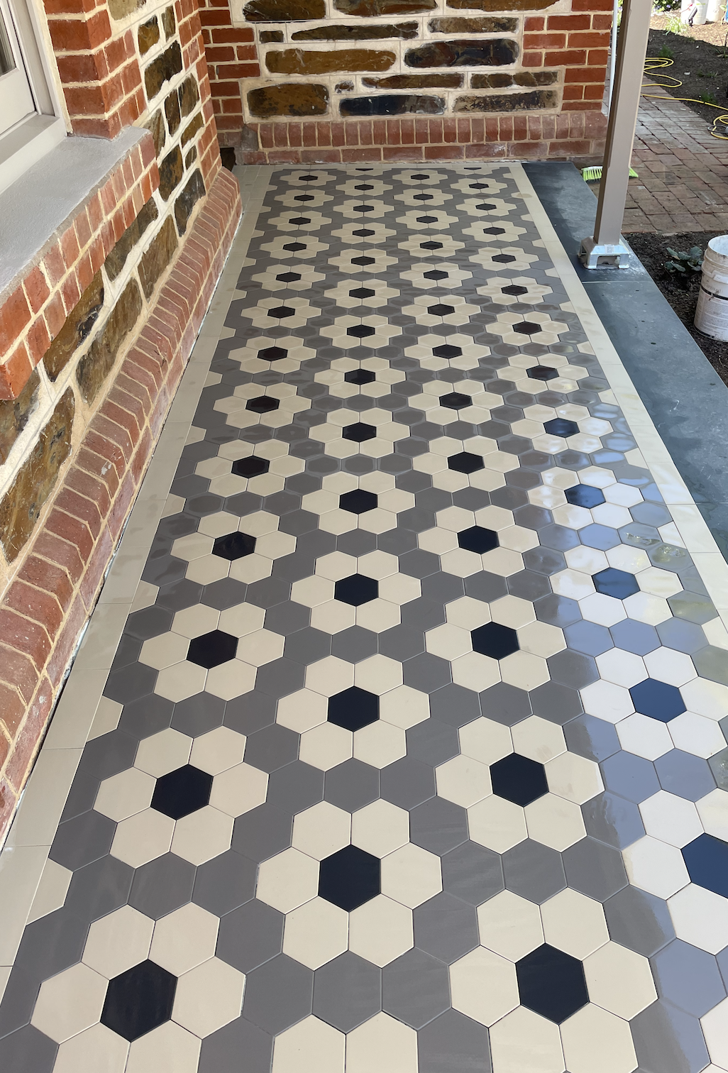 Porch flooring with geometric hexagon tile pattern in black, white, and gray tiles, adjacent to a brick wall with stones inlay.