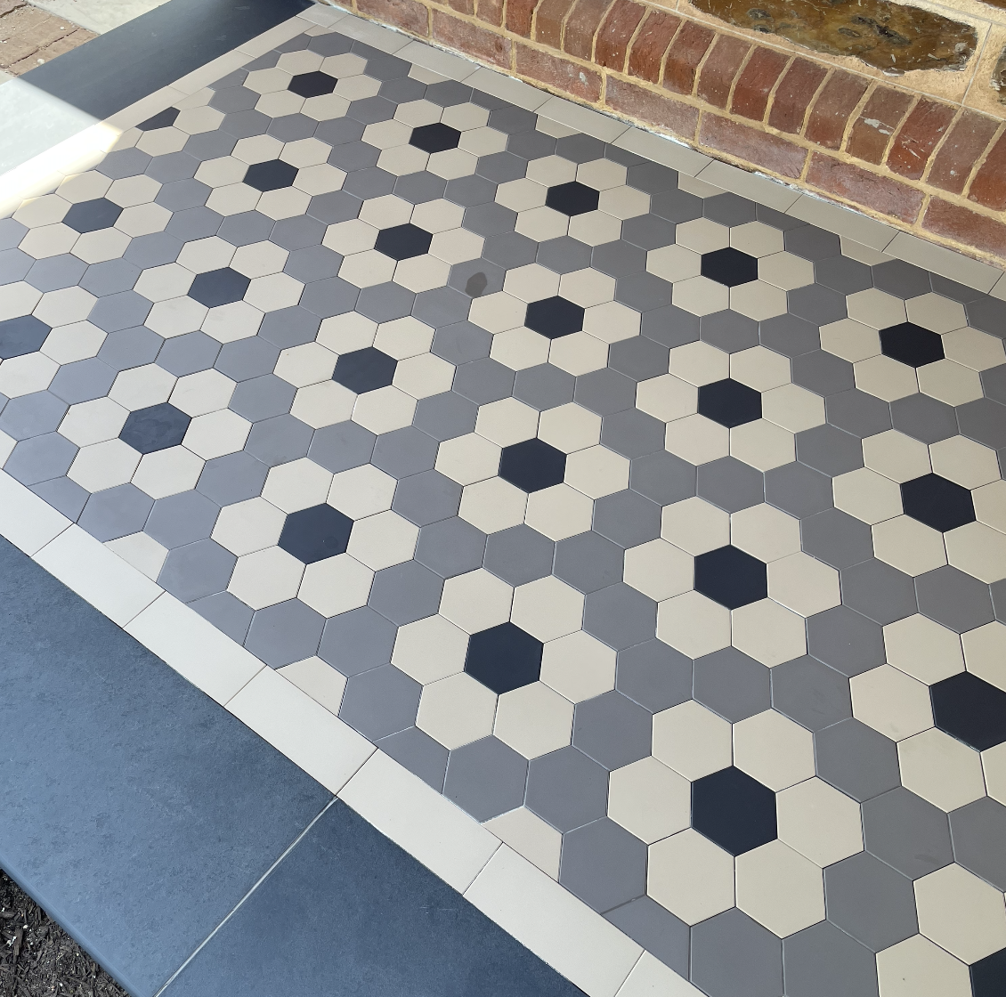 Close-up view of a patterned tile floor with hexagon tiles in black, white, and gray, next to a brick wall.