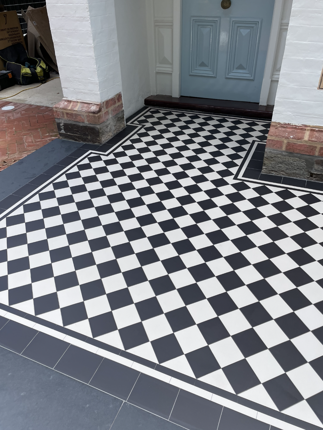 Porch with black and white checkered tile floor pattern, a light blue door, and white painted brick walls.