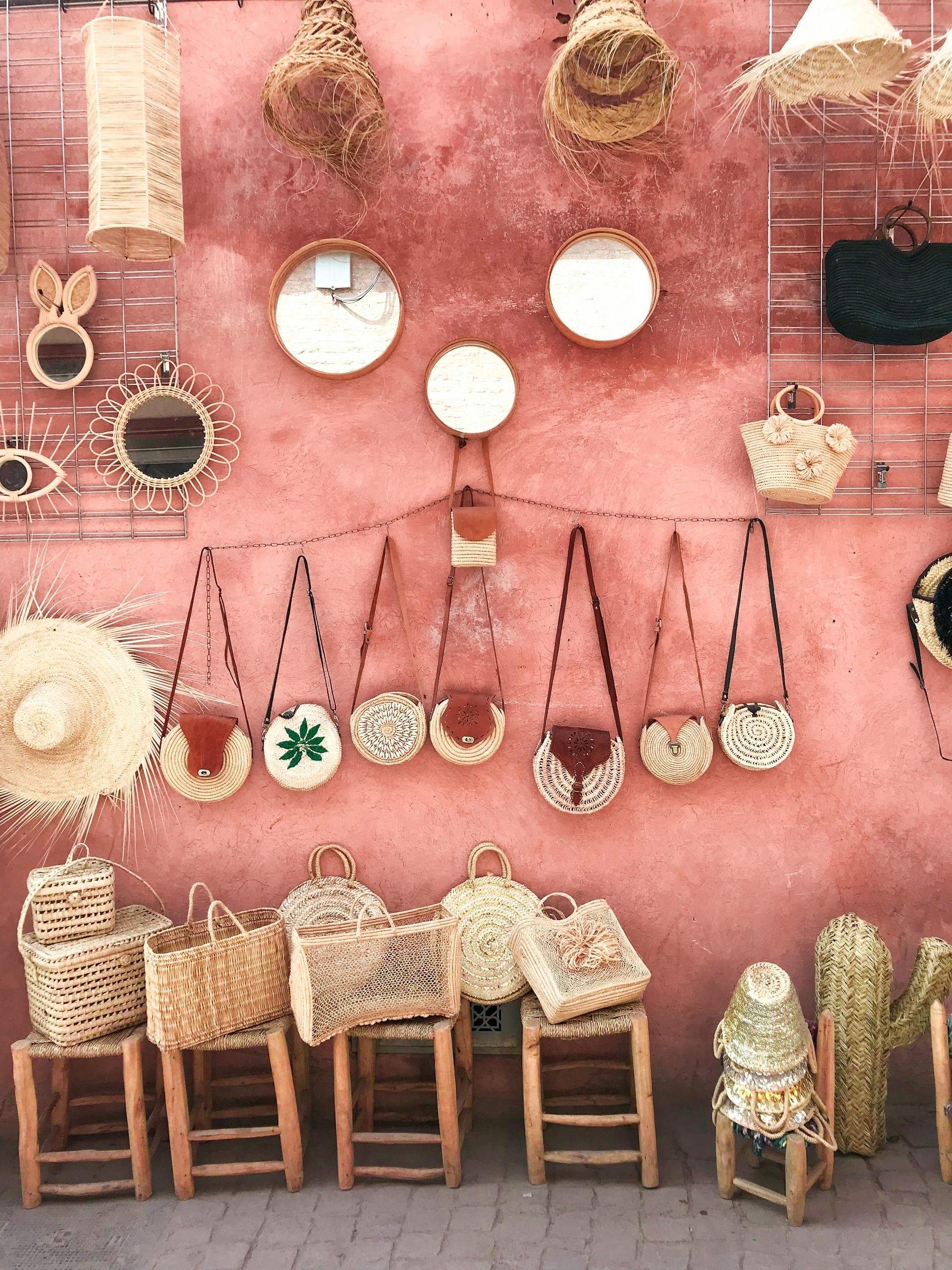 Display of woven bags, baskets, hats, and mirrors against a pink wall in a market.