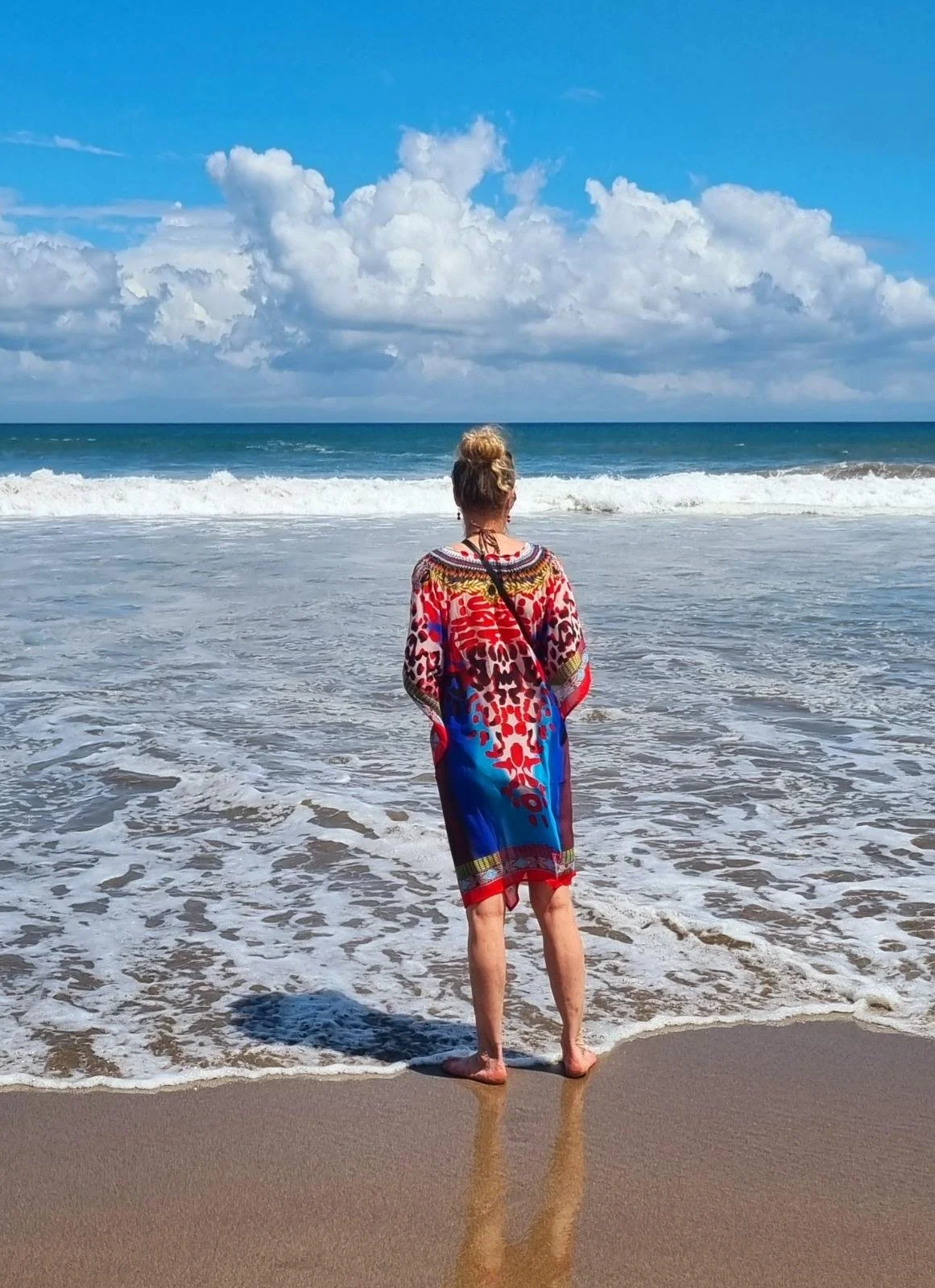Vrouw in een kleurrijke jurk kijkt uit over een zee in een rustige omgeving
