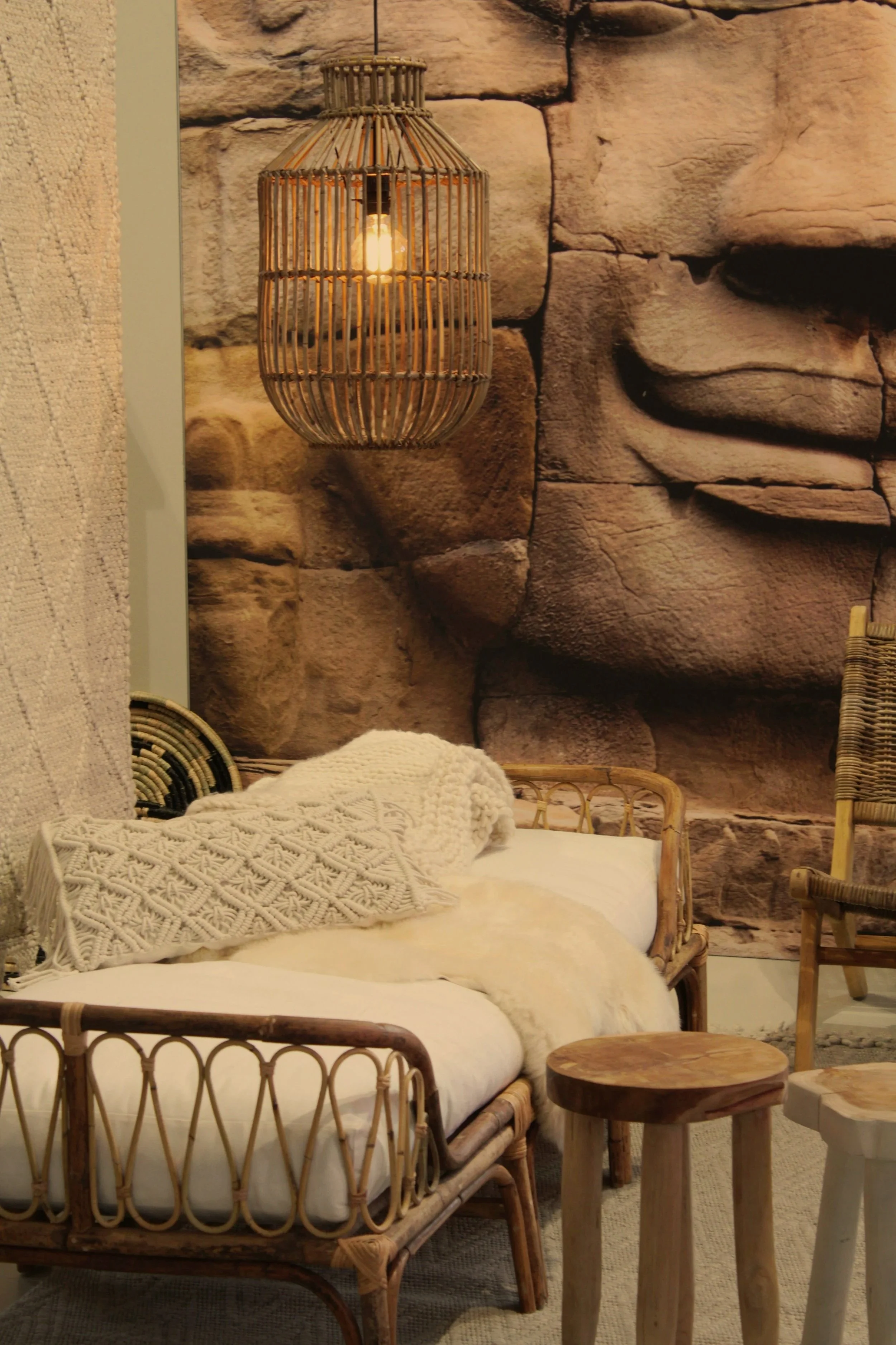 Bohemian-style interior with woven pendant light, rattan furniture, and textured pillows against a stone wall mural.