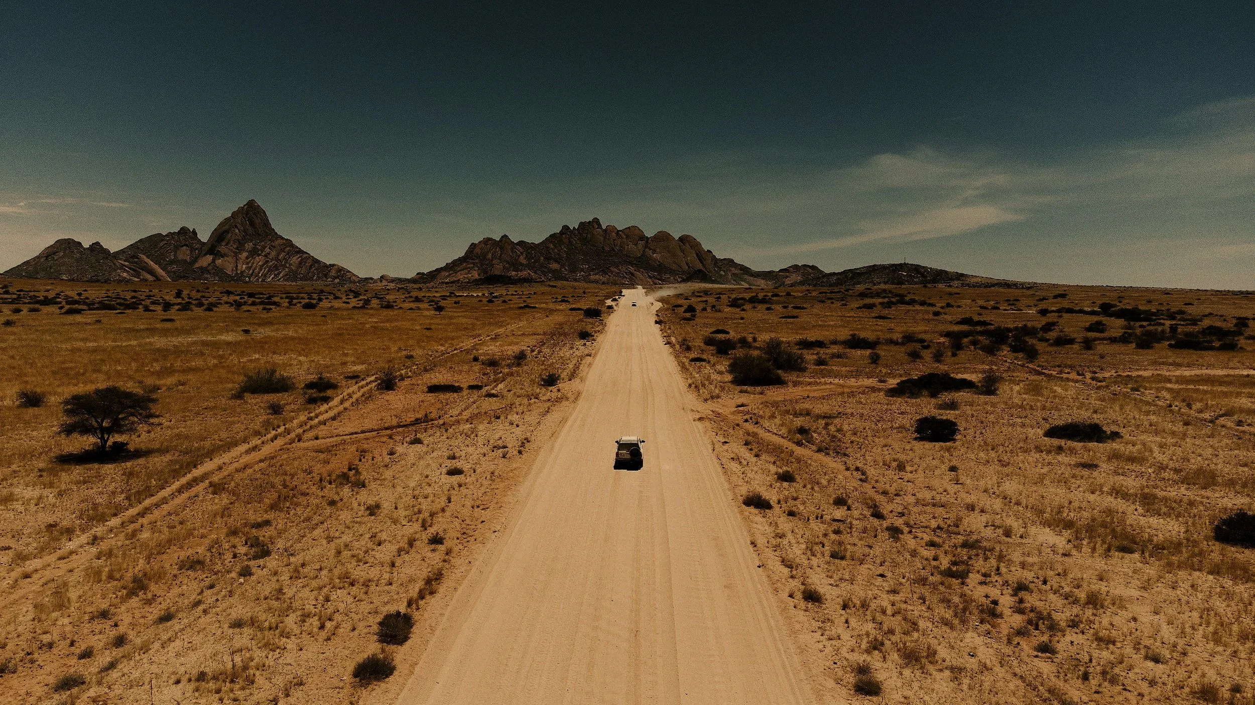 Car driving along a long straight dirt road in the Australian outback