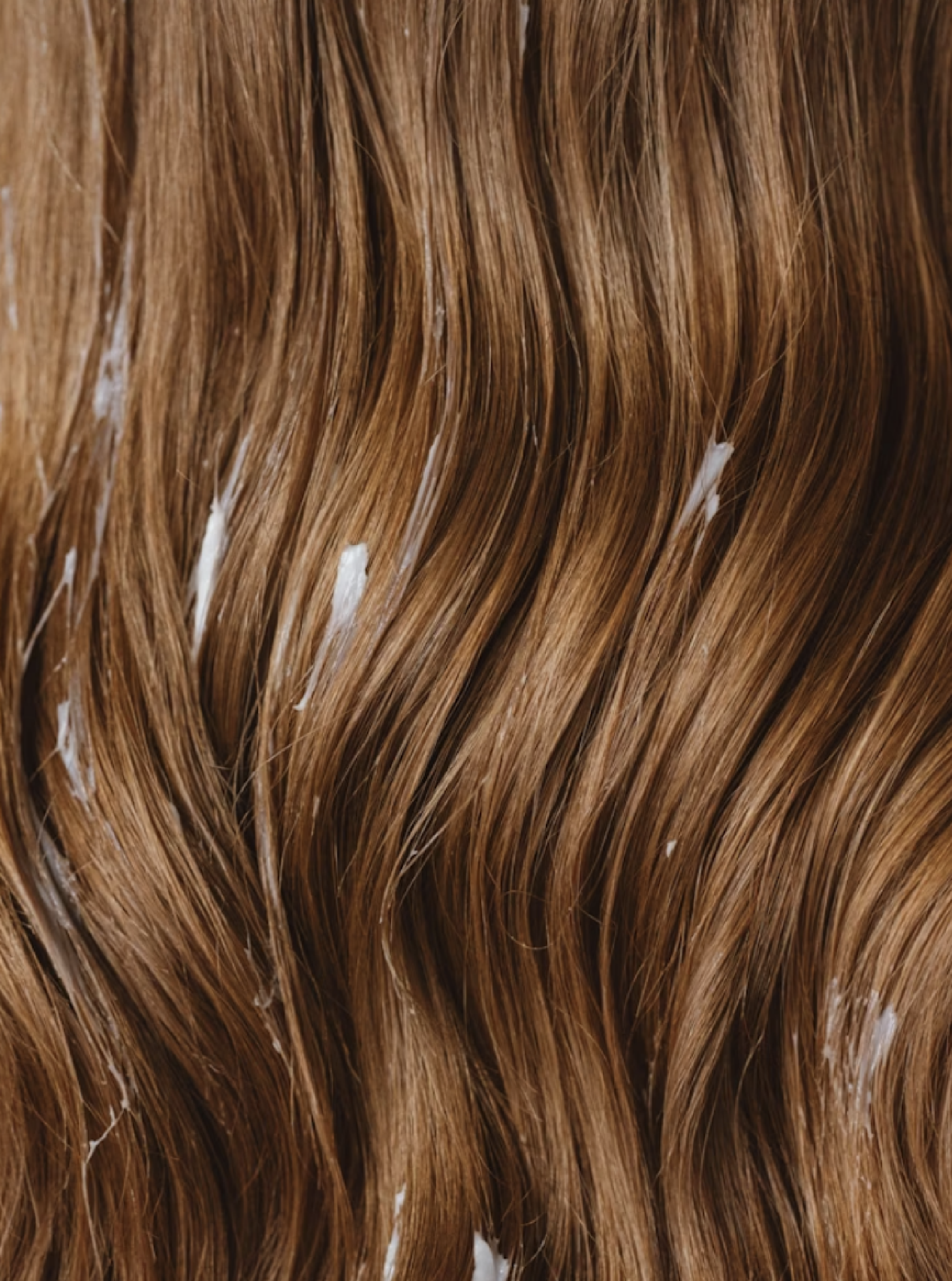 A close-up of wavy, reddish-brown hair with some white streaks.