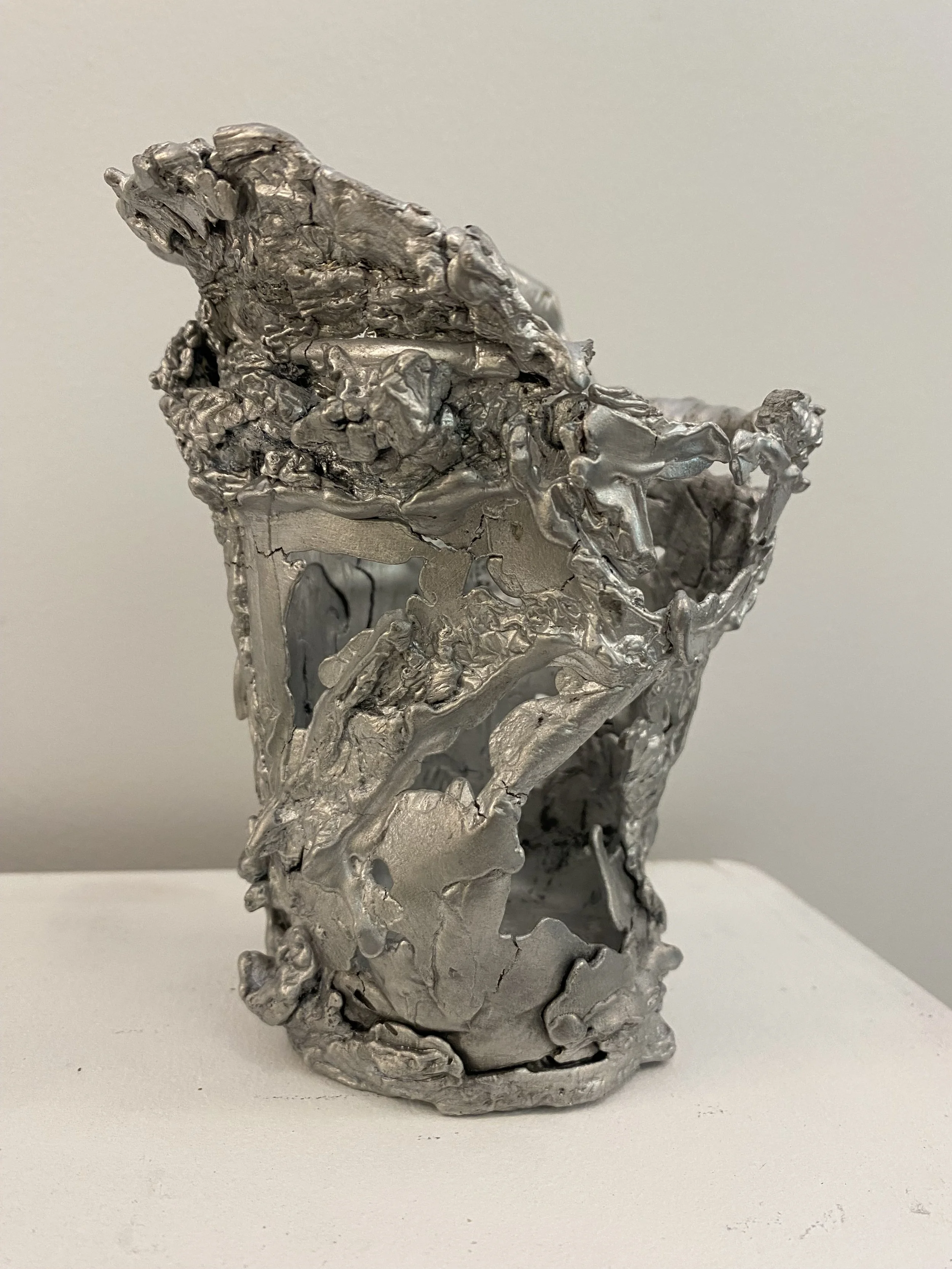 Abstract silver metal sculpture with rough, uneven, and irregular surface textures.