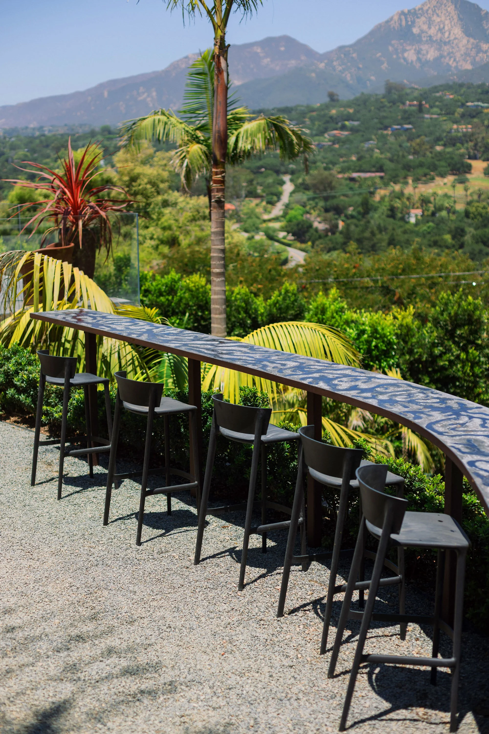 Outdoor patio with six black chairs and a curved table overlooking a lush, green landscape with mountains in the background.