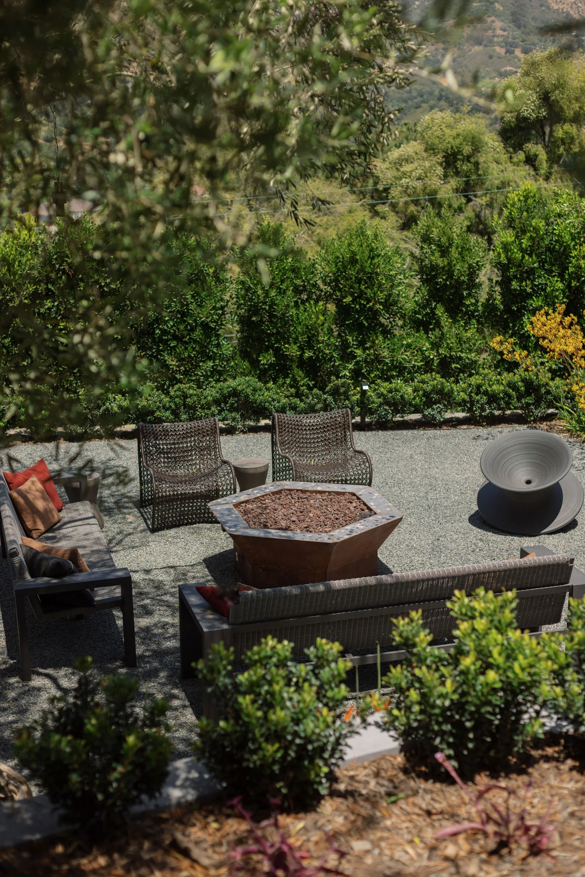 Outdoor seating area with chairs and a firepit, surrounded by greenery and scenic hills in the background.