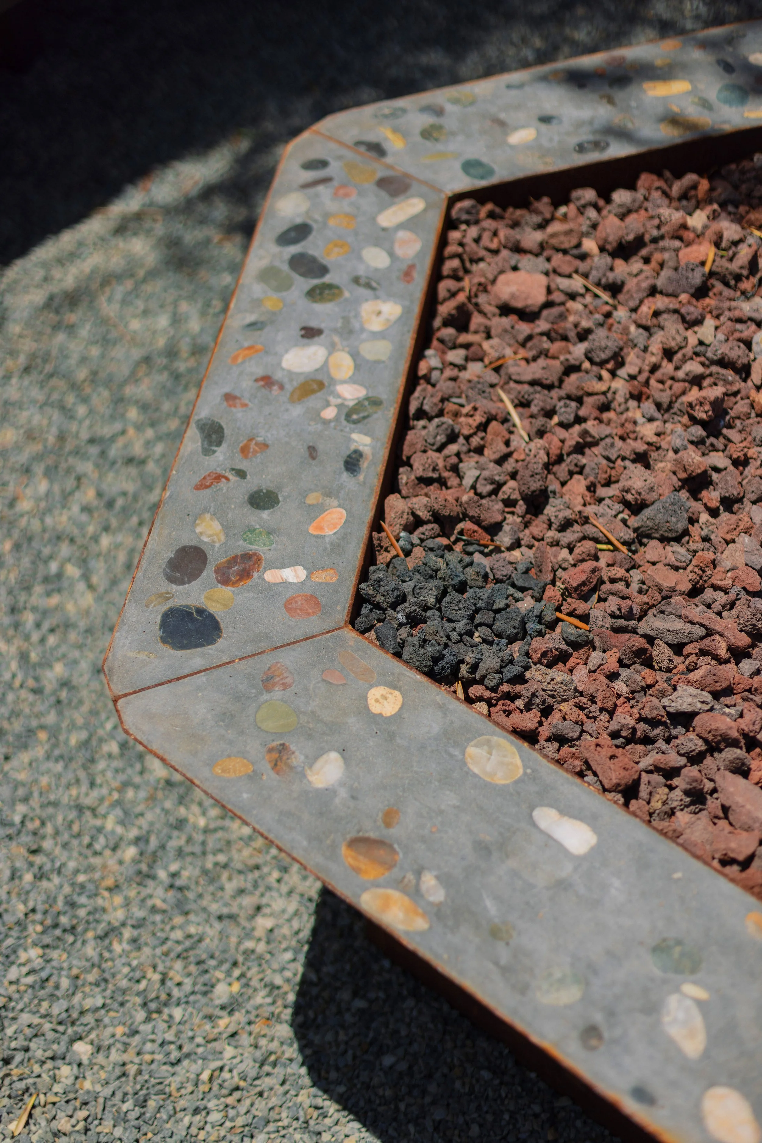 Close-up of a decorative stone border with colorful pebble accents surrounding a bed of red and black gravel.