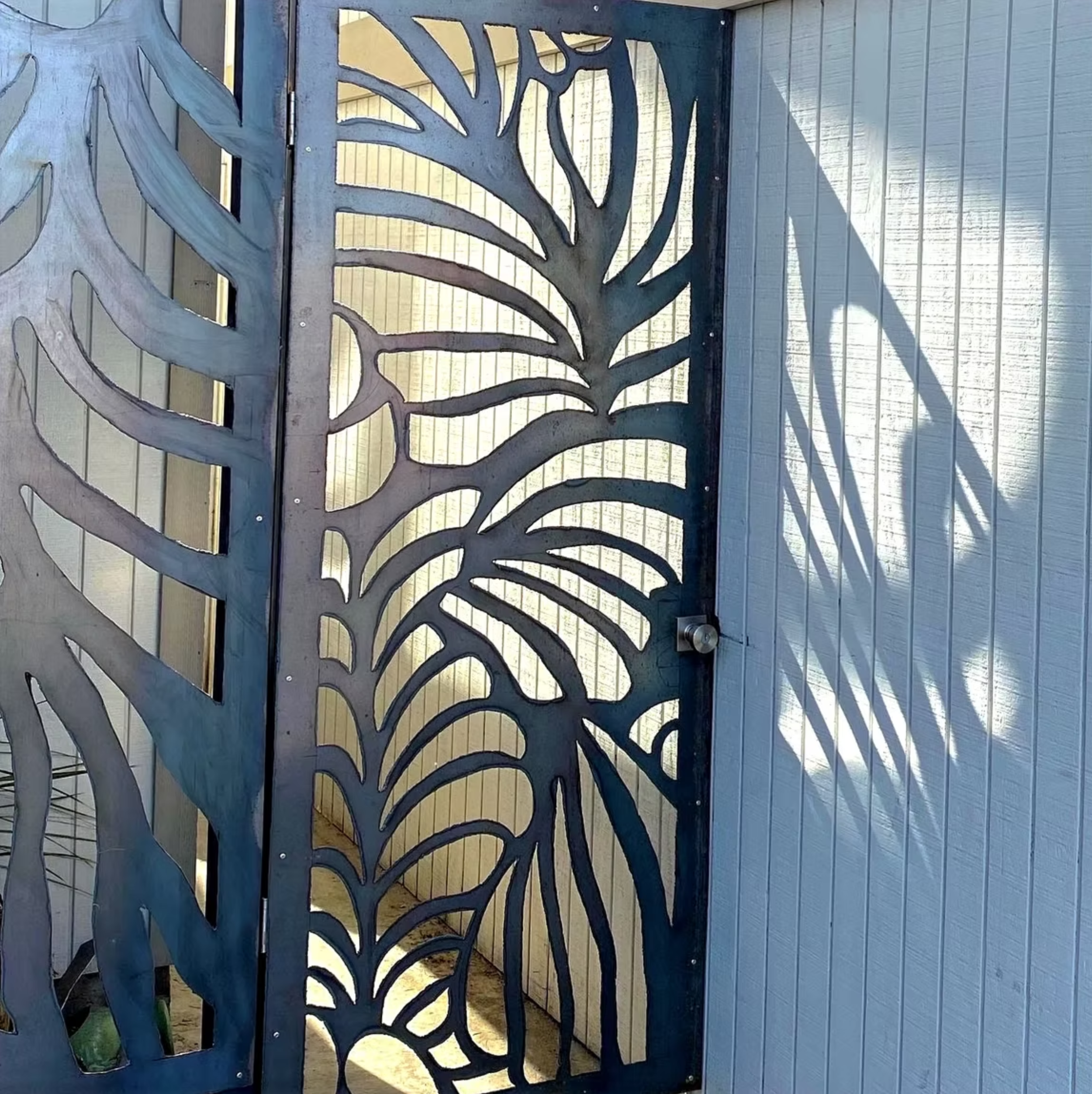 Decorative metal gate with cut-out leaf and nature-inspired design, casting shadows on a light-colored wall.