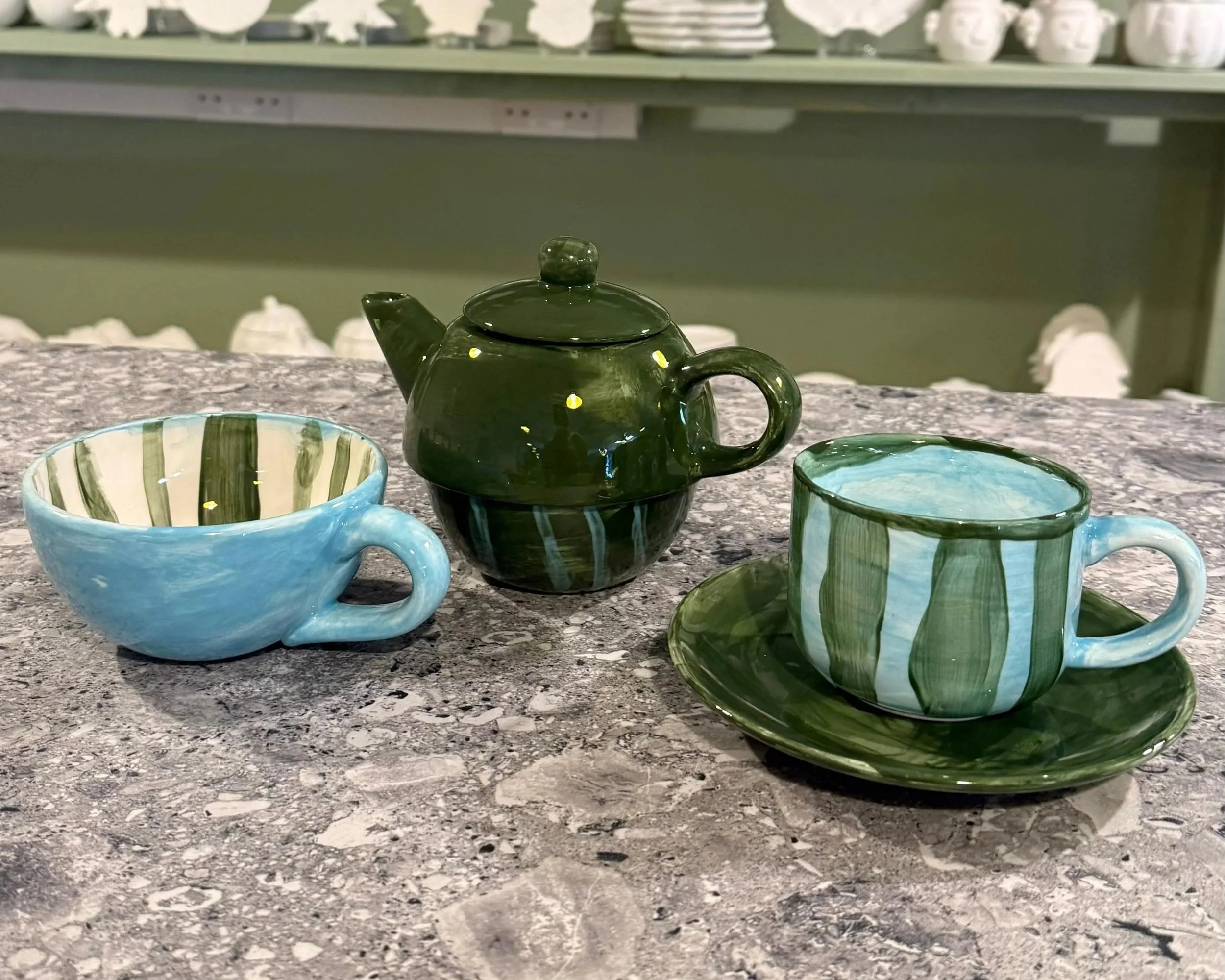 Colorful ceramic teapot and two teacups with saucers on a gray granite countertop in a store display.