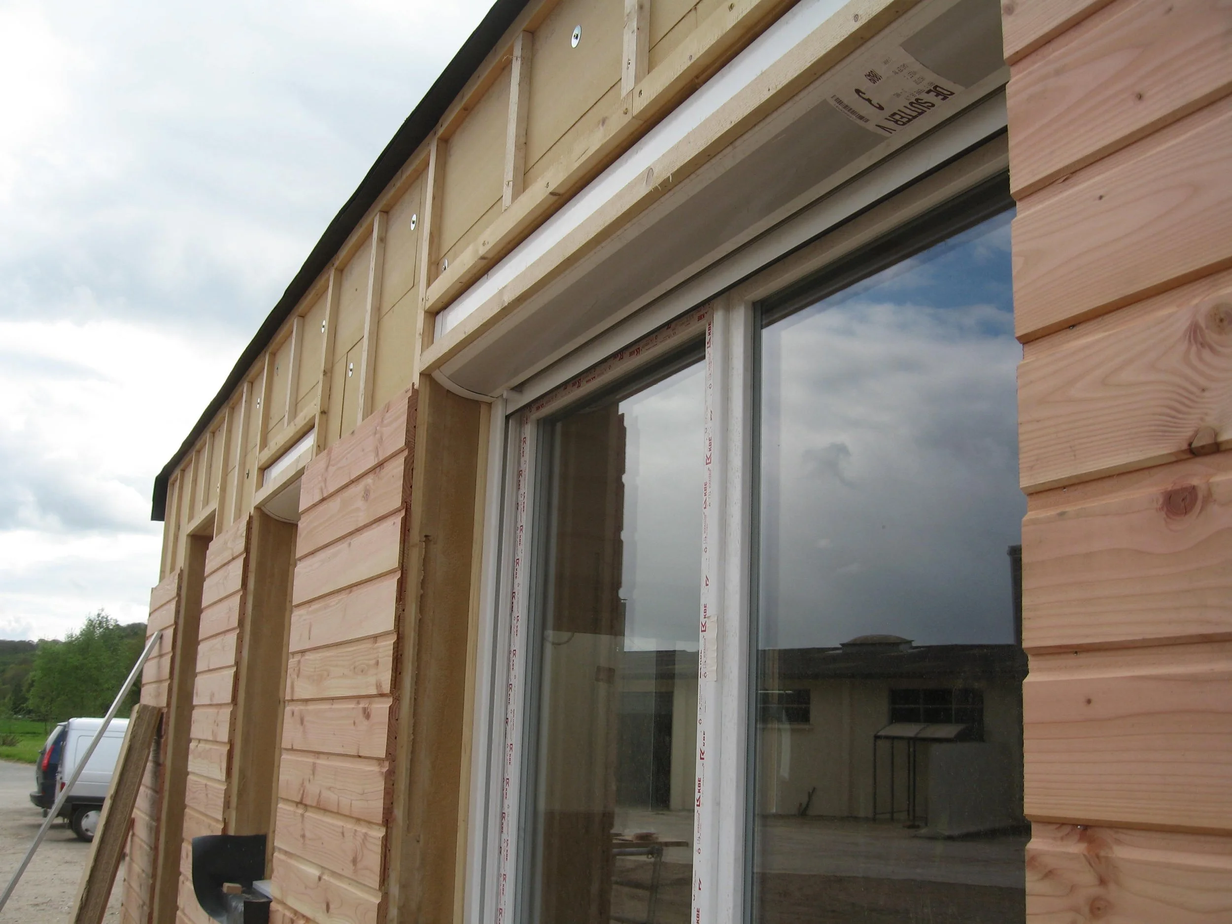 Travaux de construction d'une maison avec des murs en bois et une grande fenêtre en vitrage.