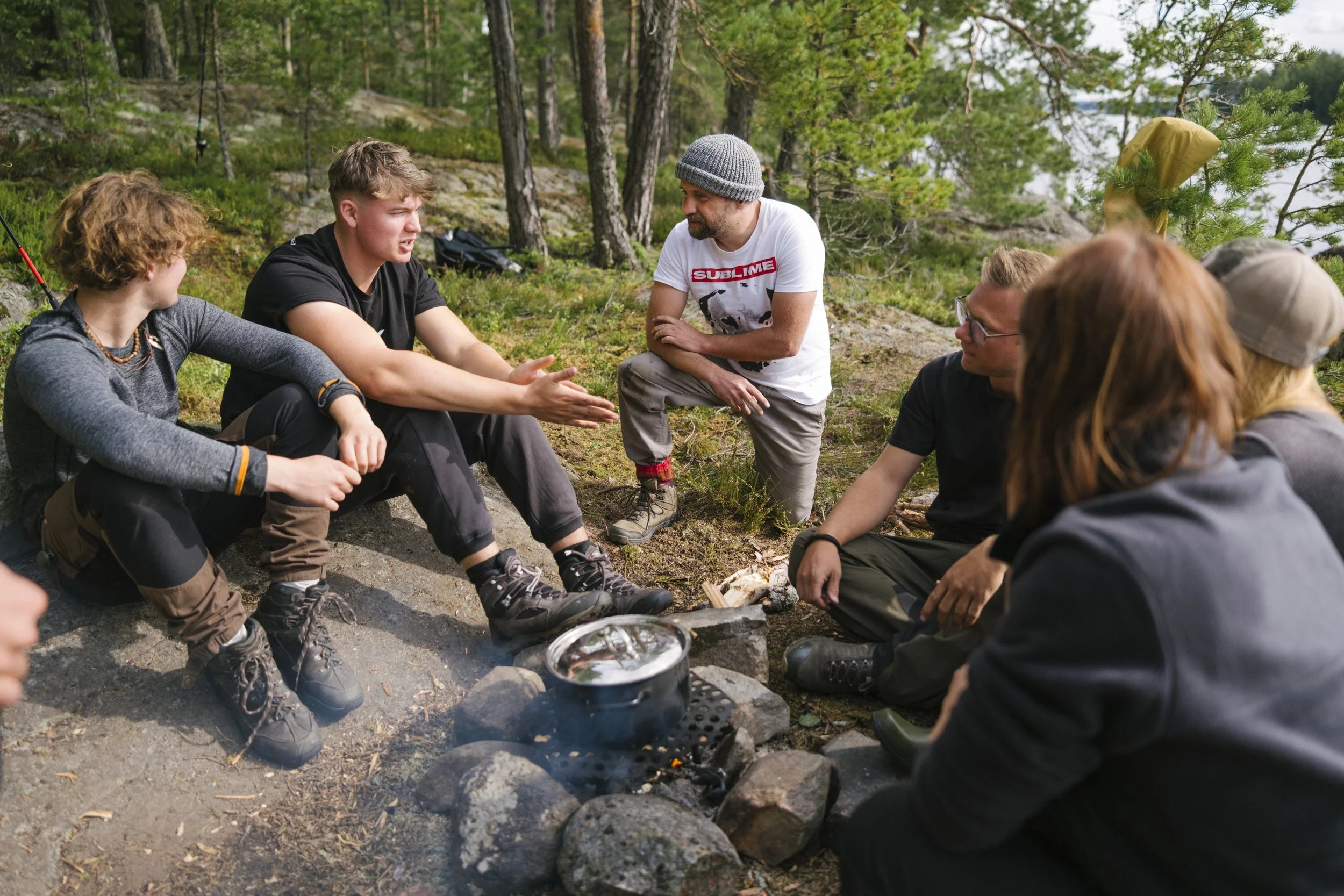 Gruppe von Menschen beim Zelten, sitzt im Kreis um ein kleines Lagerfeuer in einem Waldgebiet.