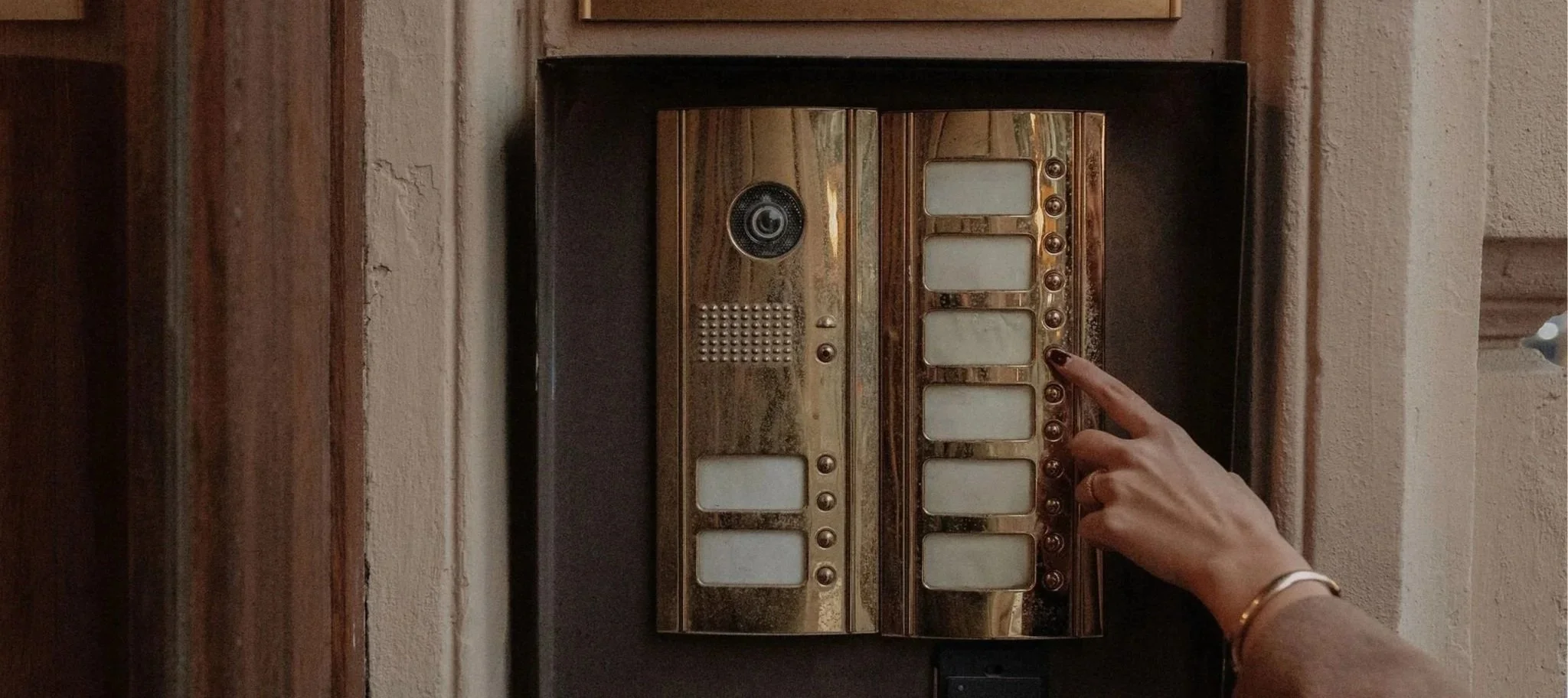 Person pressing a button on a shiny, gold-colored intercom at an apartment door.