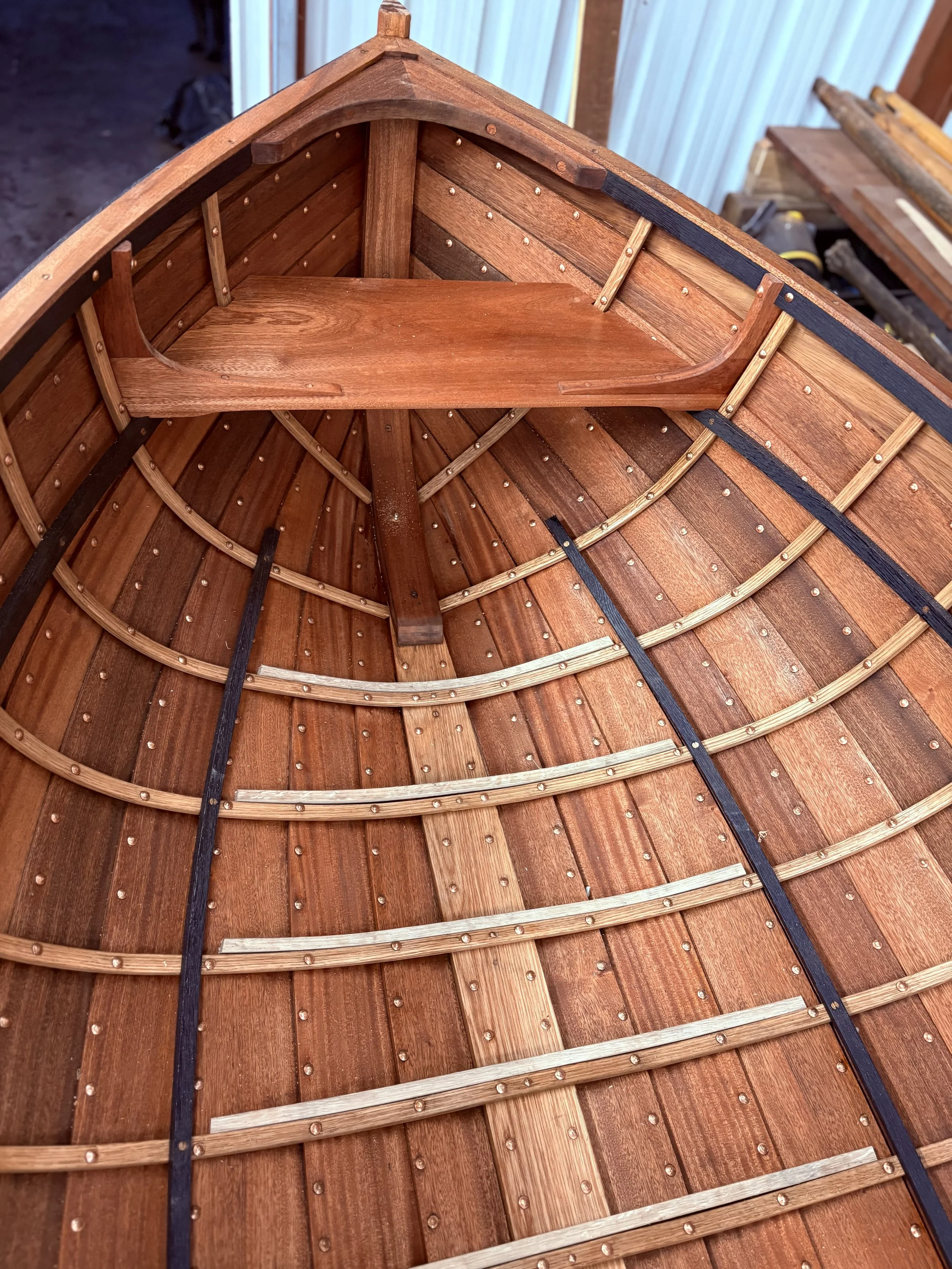 The interior of a wooden boat under construction, showing the framework, planking, and seating area.