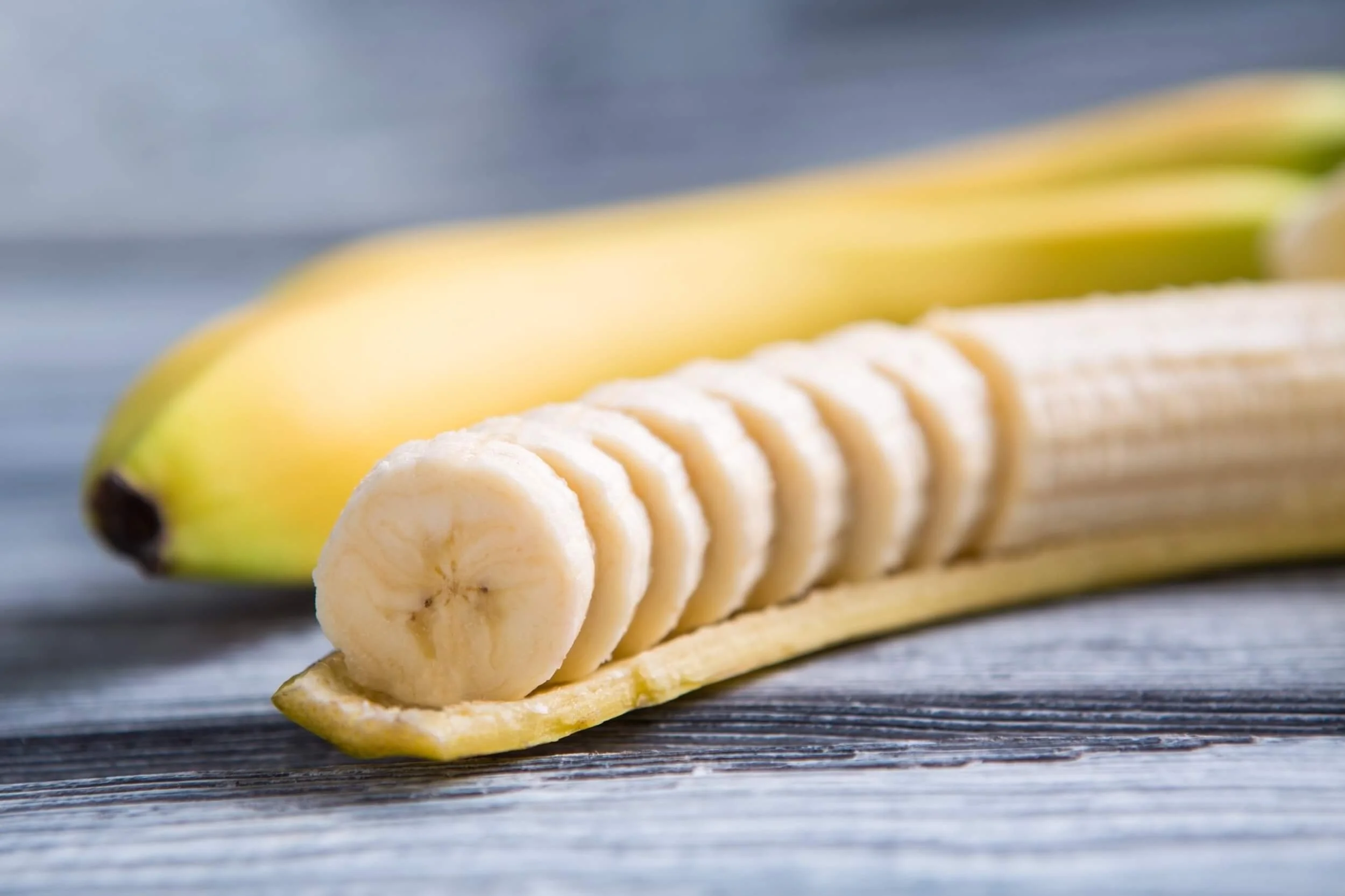 Sliced banana on a wooden surface with whole banana in the background.