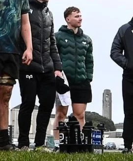 Group of people standing outdoors near a monument, with water bottles on the grass in front of them.
