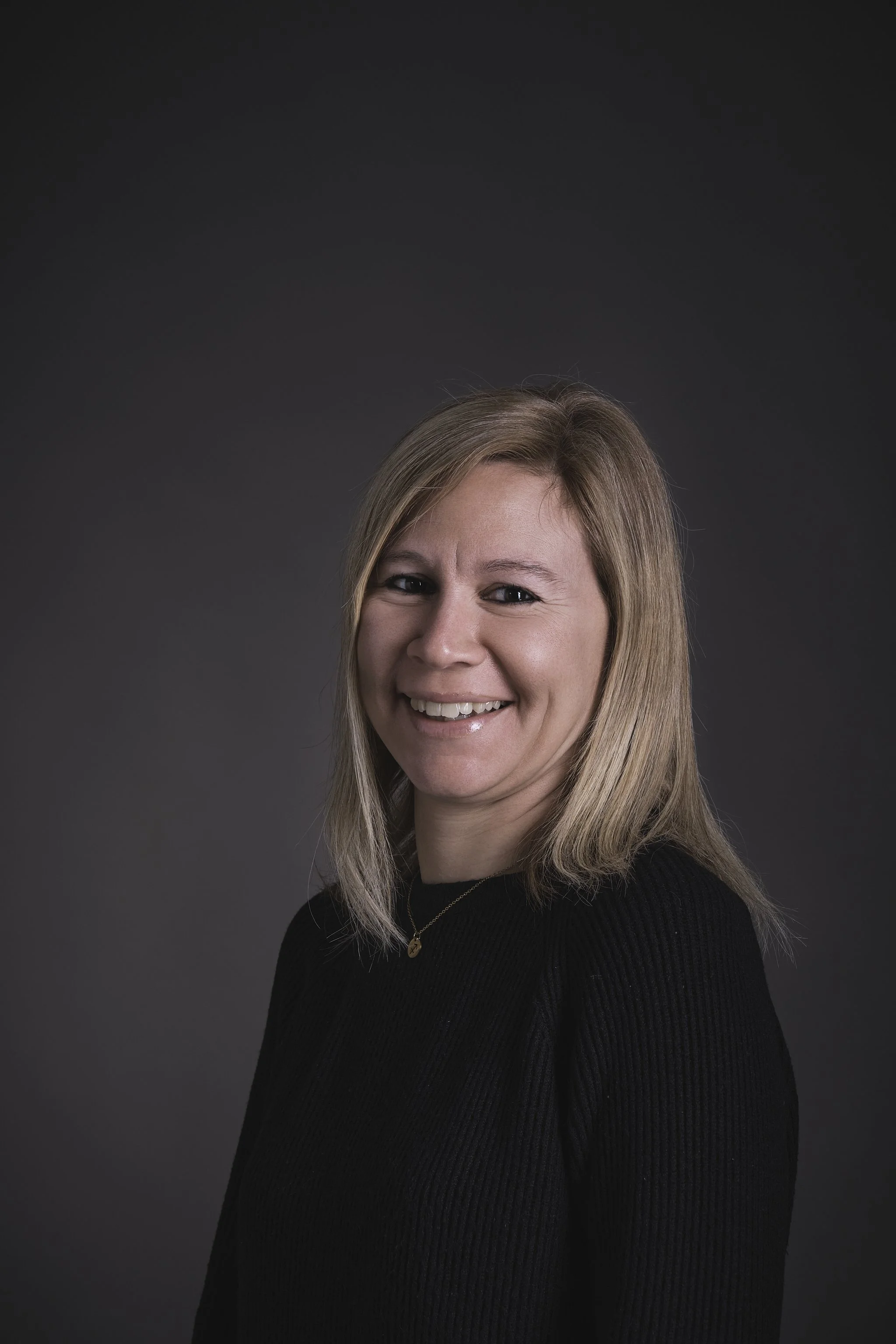 Una giovane donna sorride sorridendo, indossa un maglione rosso e ha capelli lunghi e ondulati.