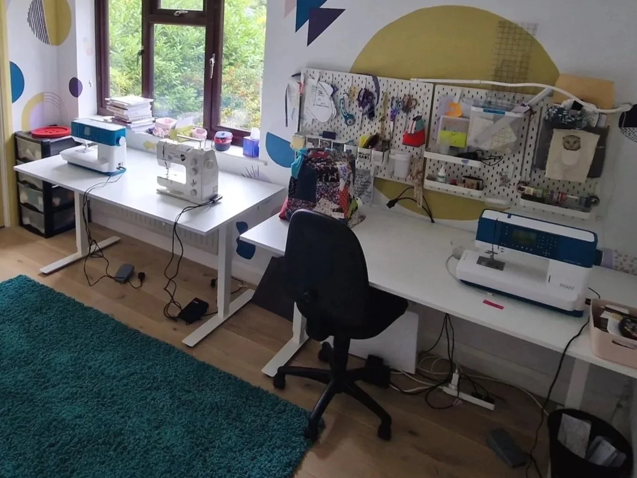 Two desks against a wall with sewing machines on the desks.