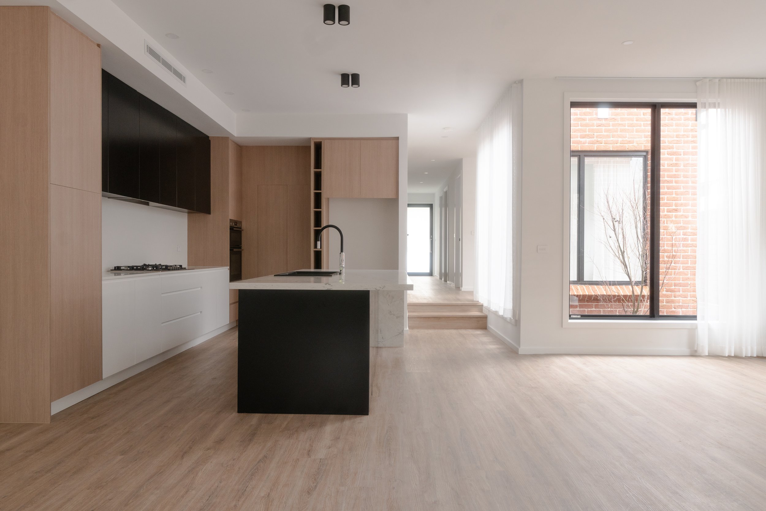 Empty, modern, open-concept kitchen and living space with large windows, wood flooring, and minimal decor.