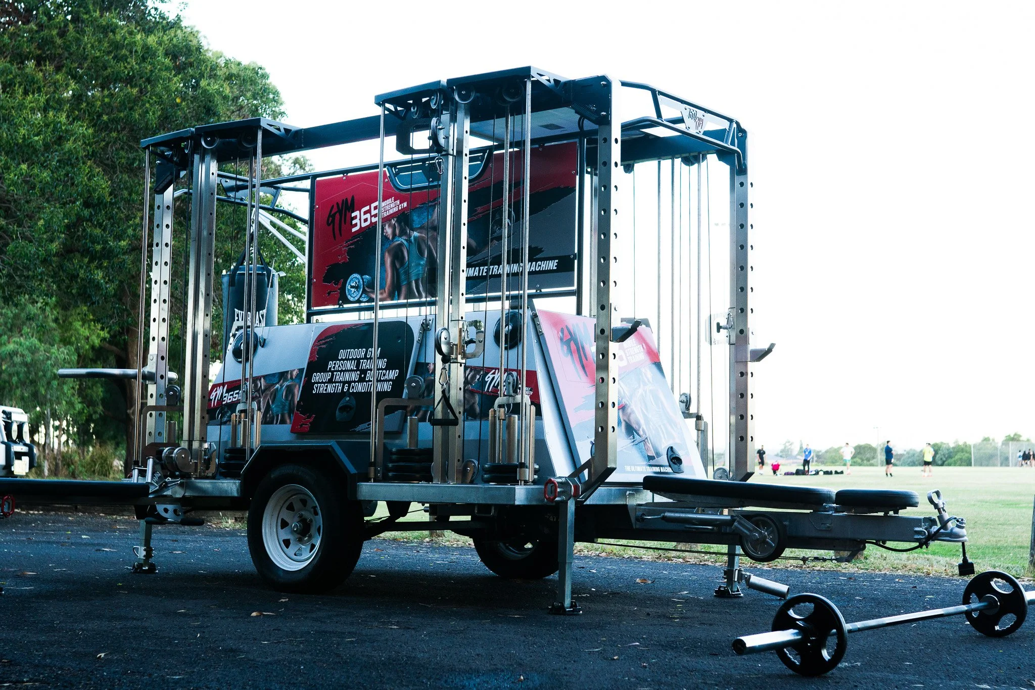 Mobile gym trailer with workout equipment and promotional banners at an outdoor sports field