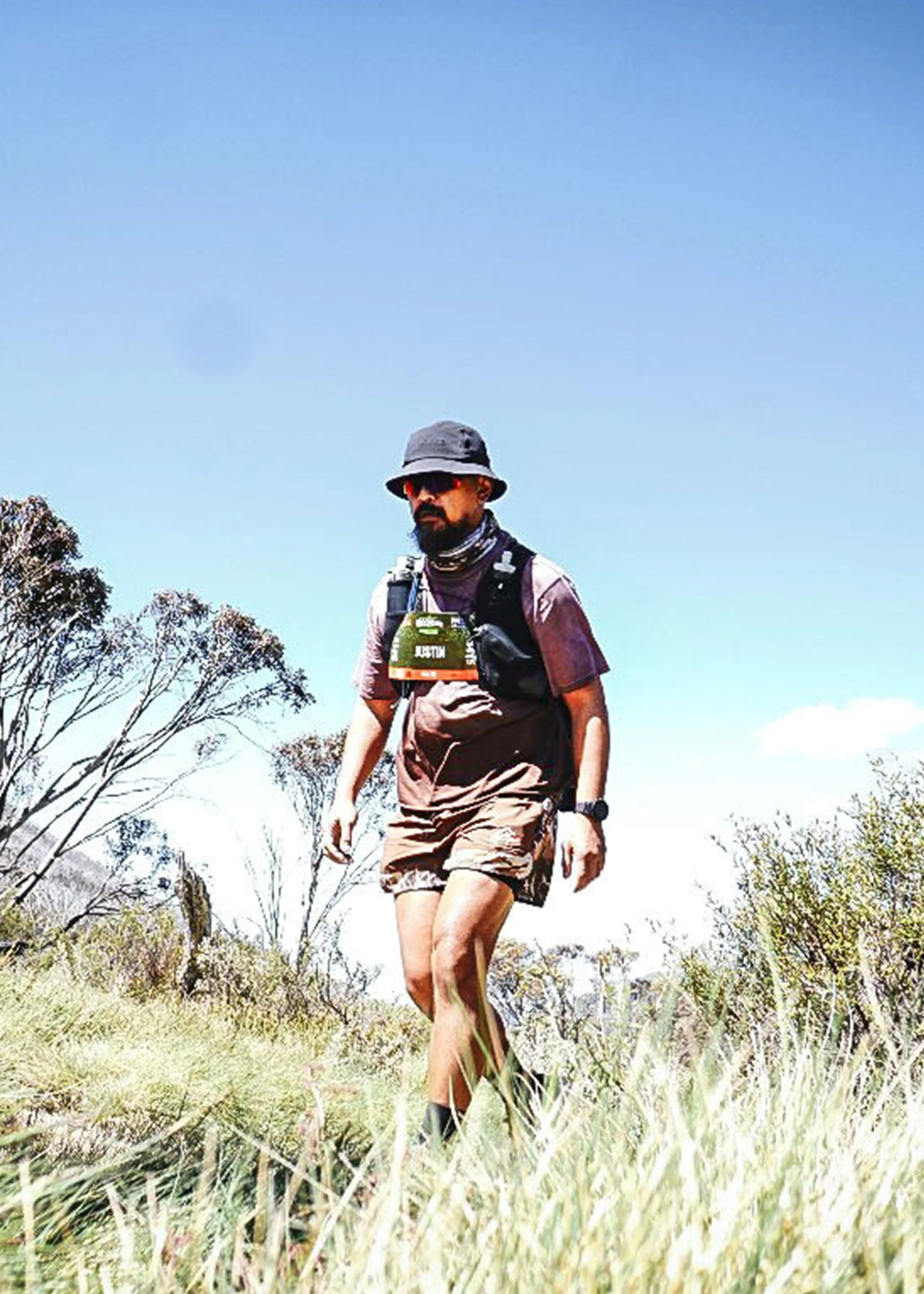 A person hiking outdoors in a grassy area with trees and a blue sky.