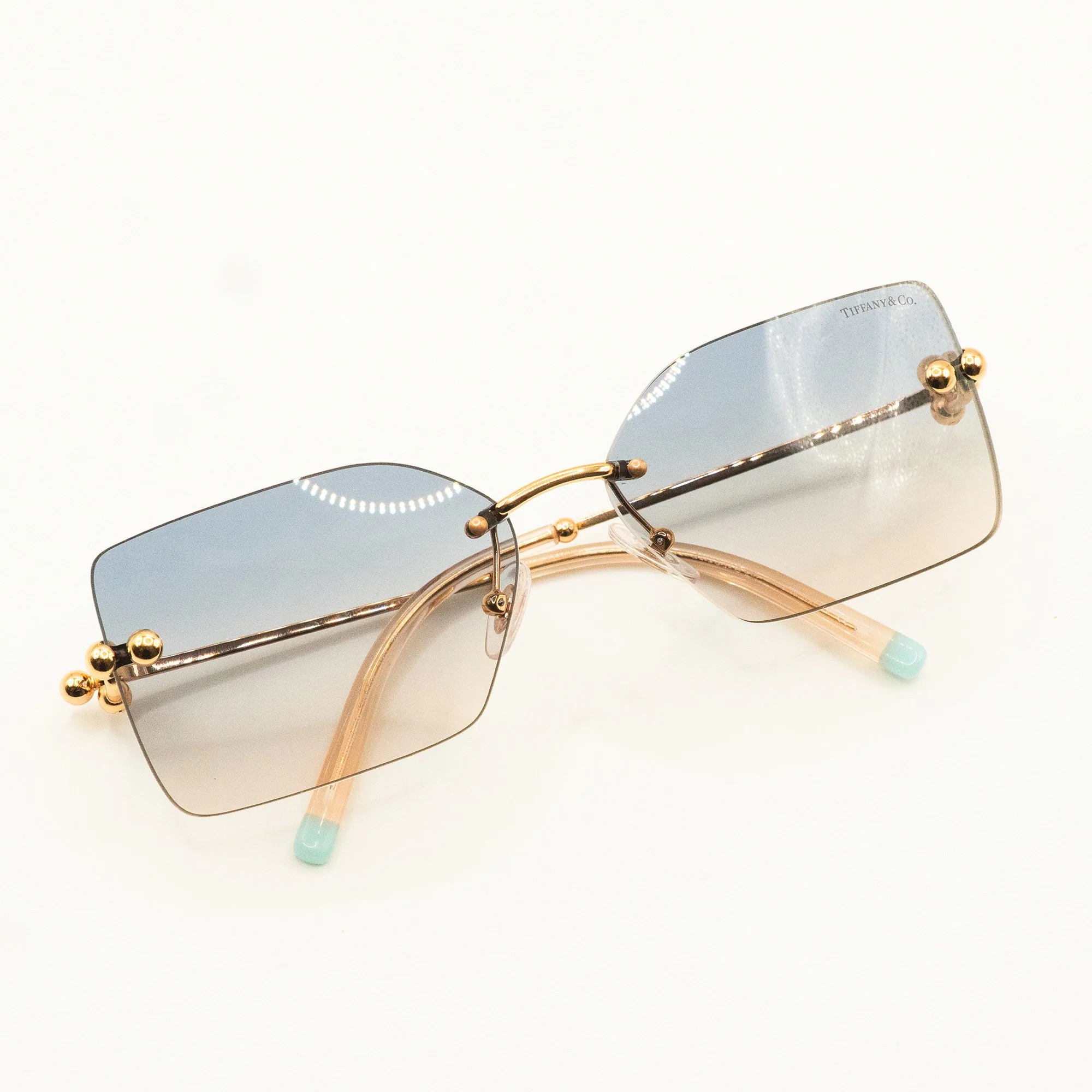 Pair of Tiffany & Co. sunglasses with rectangular blue-tinted lenses, gold accents, and pinkish nose pads, placed on a plain white background.